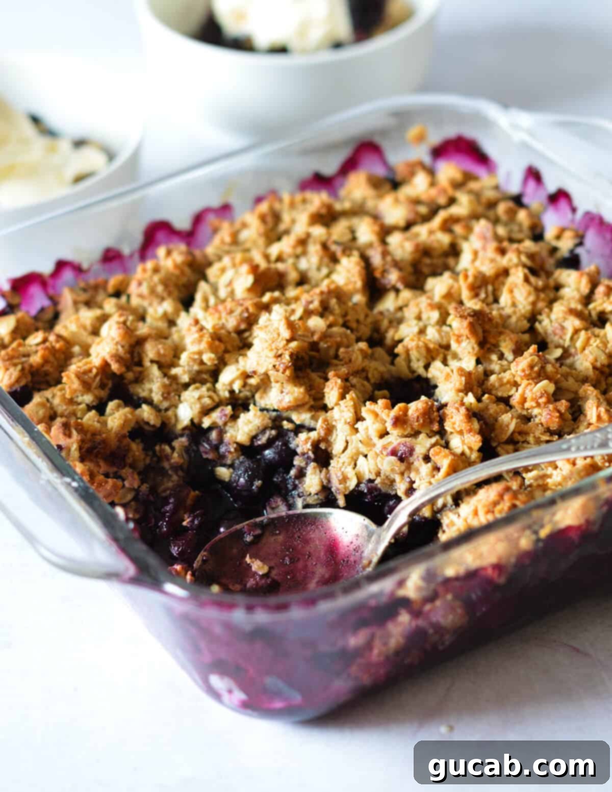 A golden-brown healthy blueberry crisp with a spoon scooping out a portion, showcasing the jammy filling and crispy topping.