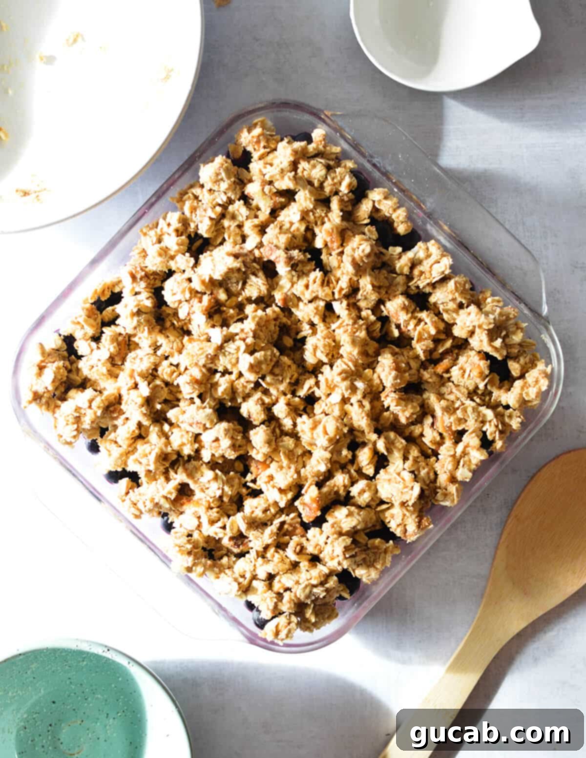 An unbaked blueberry crumble, with the topping evenly spread over the blueberries in the baking dish.
