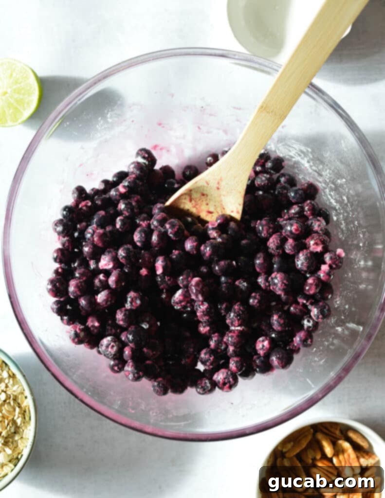 A bowl of frozen blueberries mixed with maple syrup, lime juice, and tapioca flour, forming a glossy filling.