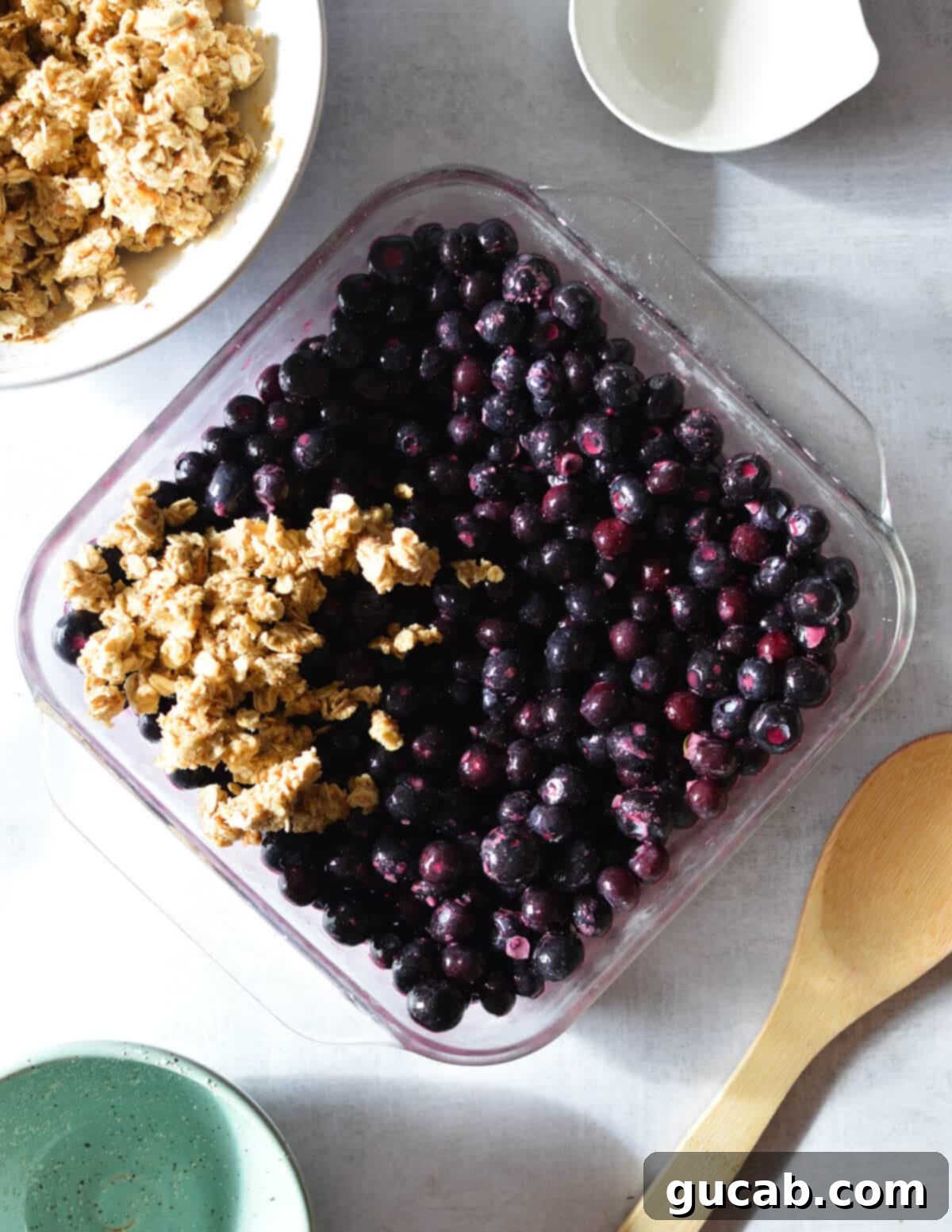 A baking dish with blueberries, with a pile of crumble topping in one corner, ready to be spread.