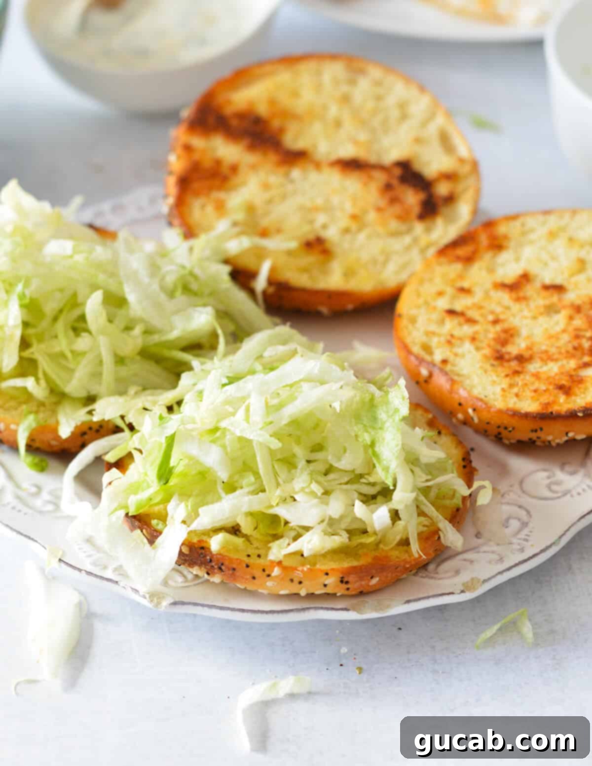 Toasted brioche bottom buns topped with a bed of shredded iceberg lettuce.