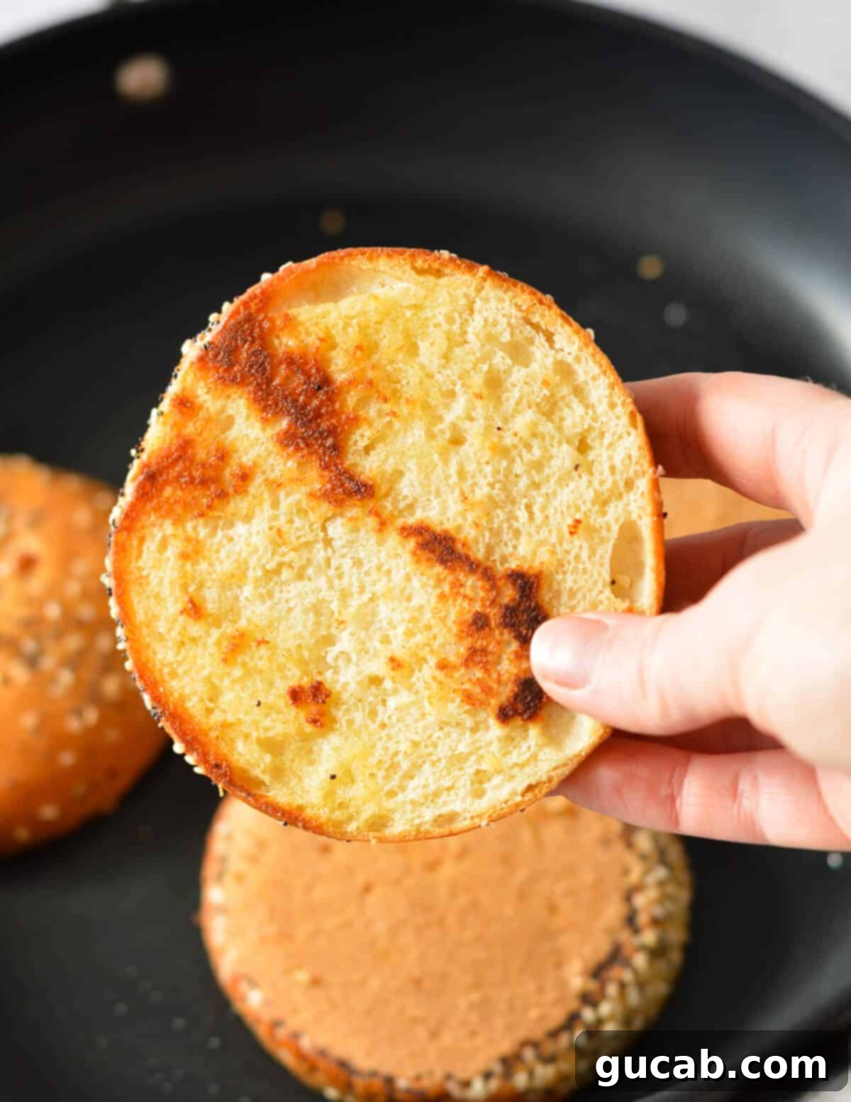 A hand holding a perfectly toasted brioche bun, showing its golden-brown interior.