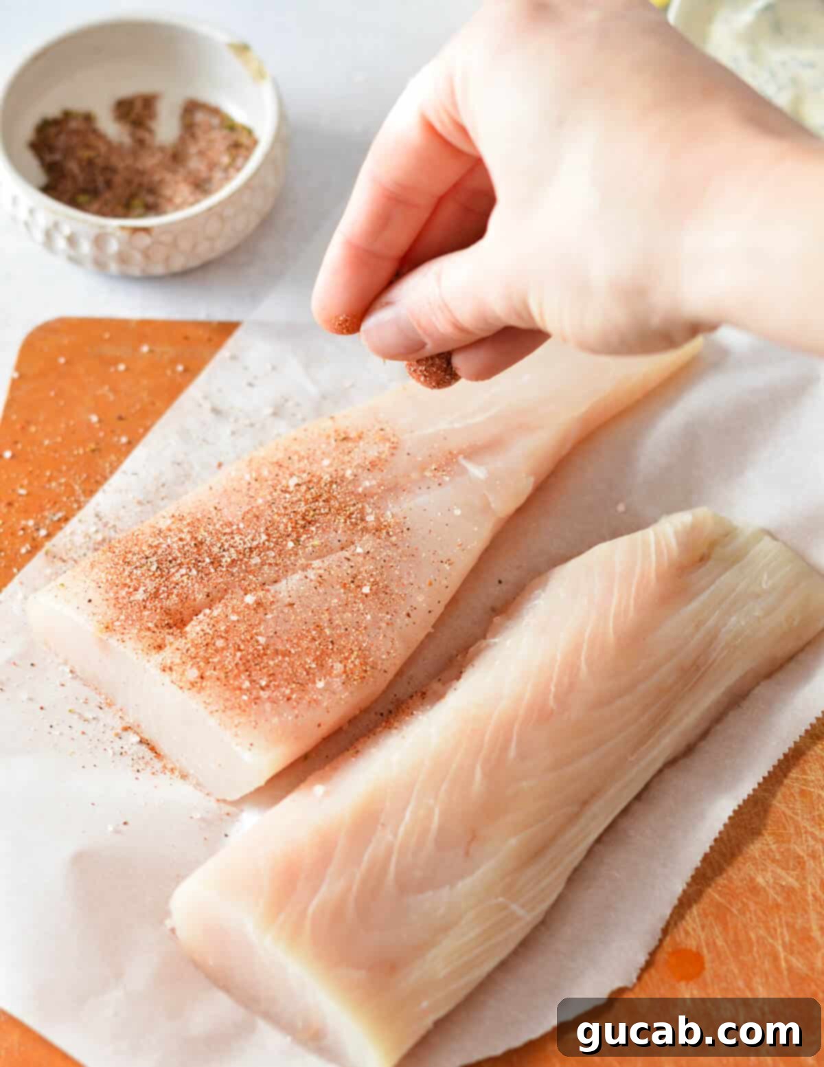 A hand sprinkling a generous amount of blackening seasoning onto mahi mahi fillets.