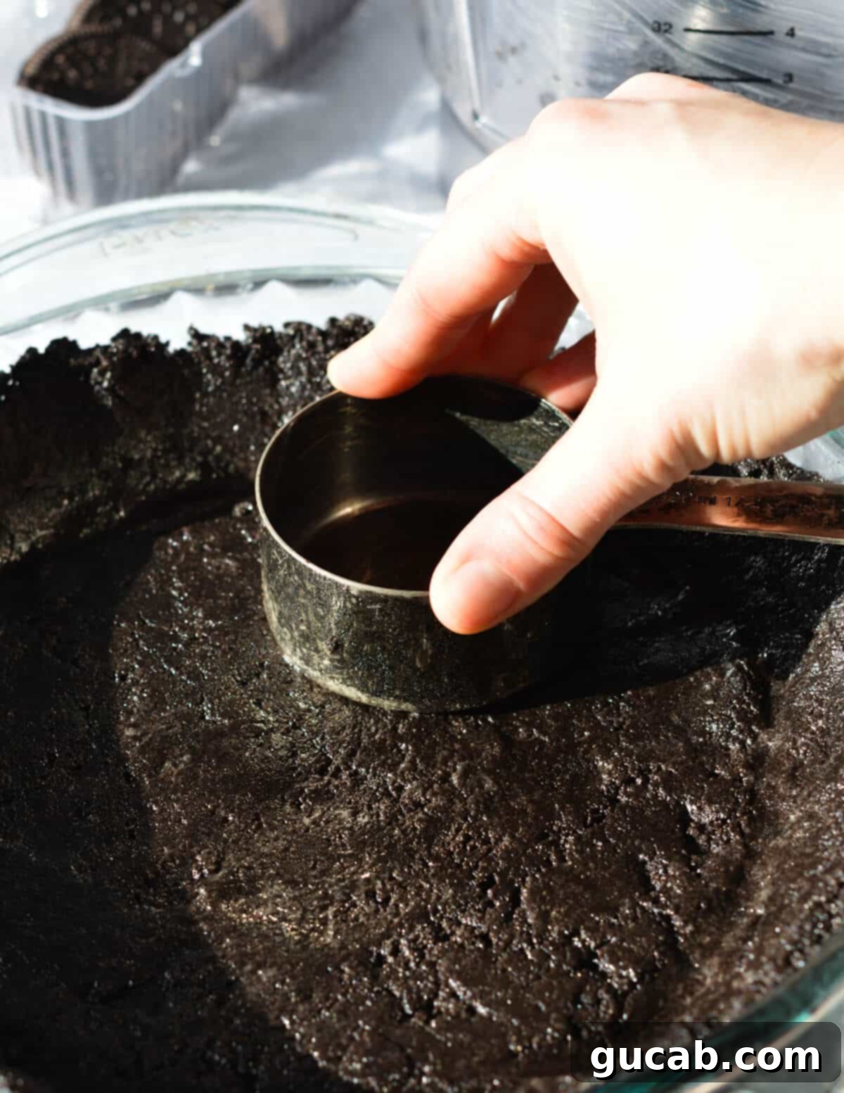 The Ultimate Gluten-Free Oreo Pie Crust 10 hand pressing a cookie crust into a pan with a measuring cup.