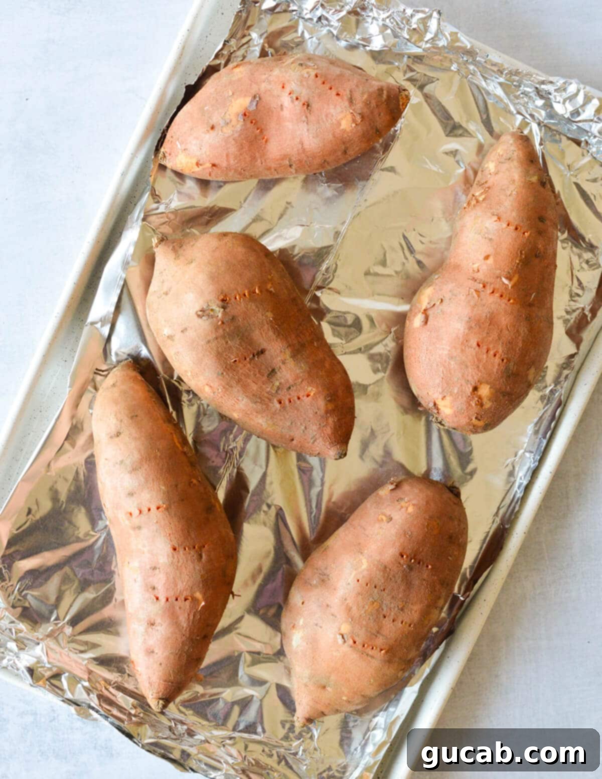 Heavenly Sweet Potato Casserole 4 Raw sweet potatoes on an aluminum foil-lined sheet pan, poked with a fork, ready for baking.