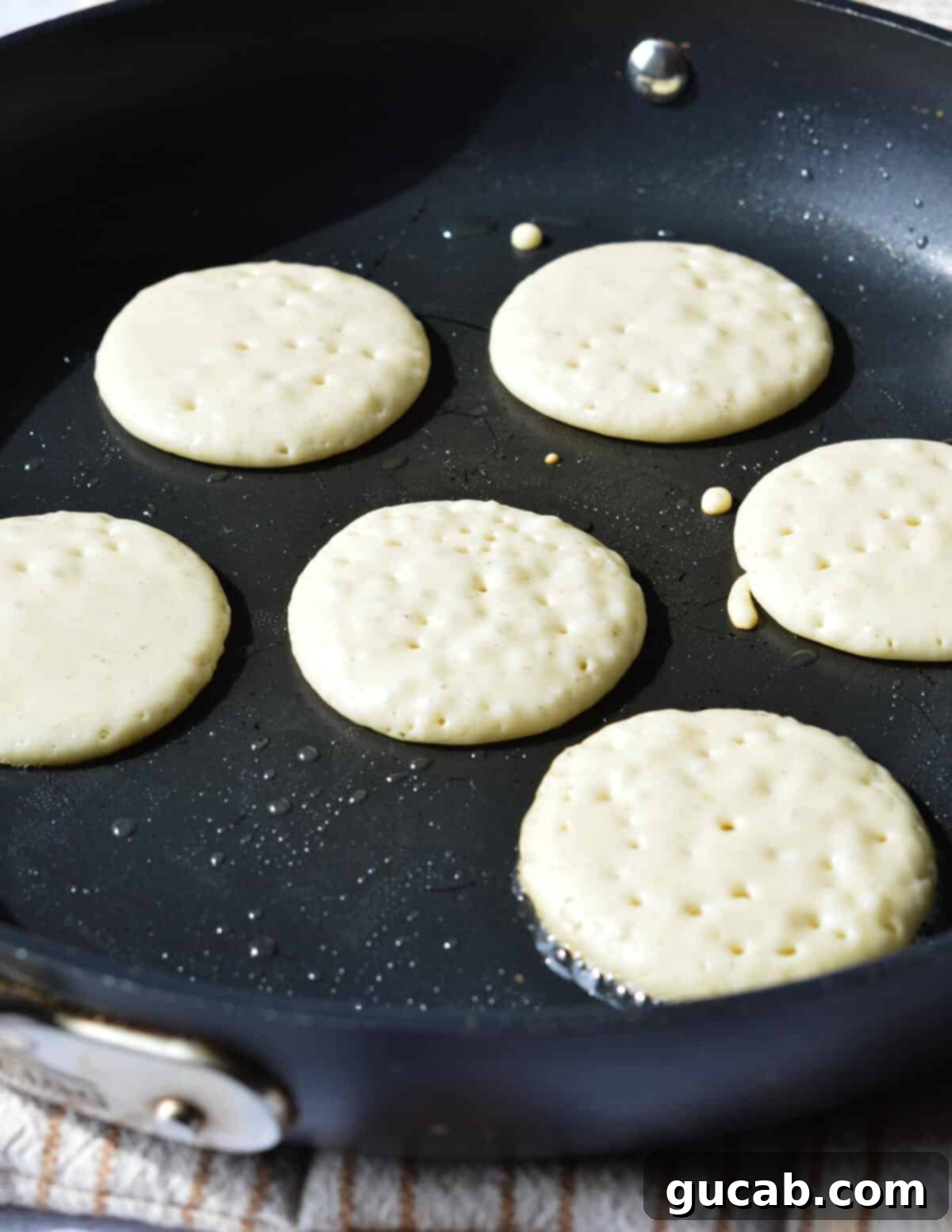 small pancakes cooking in a skillet with many bubbles forming on the surface.