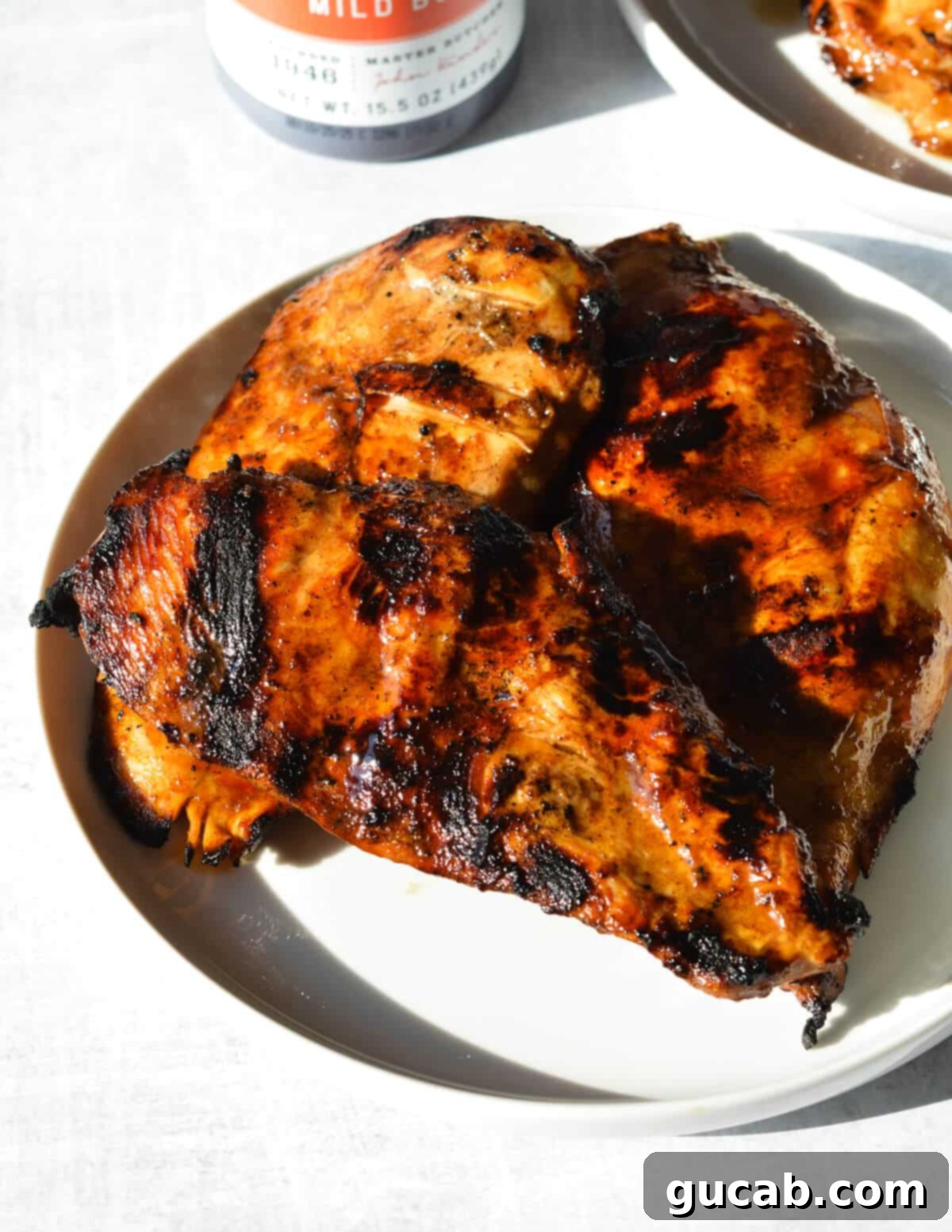 Perfectly grilled chicken breasts resting on a white plate, showcasing a beautiful caramelized exterior and juicy texture, garnished with fresh herbs.