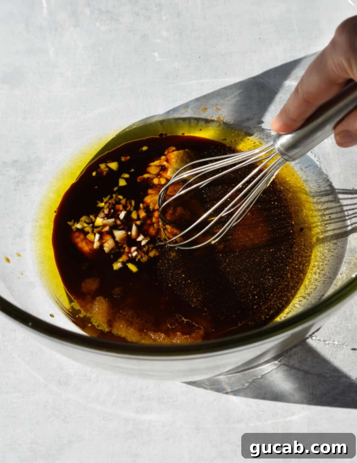 A bowl filled with all the liquid marinade ingredients before whisking: olive oil, balsamic vinegar, brown sugar, Dijon mustard, and garlic, showcasing the separate layers.