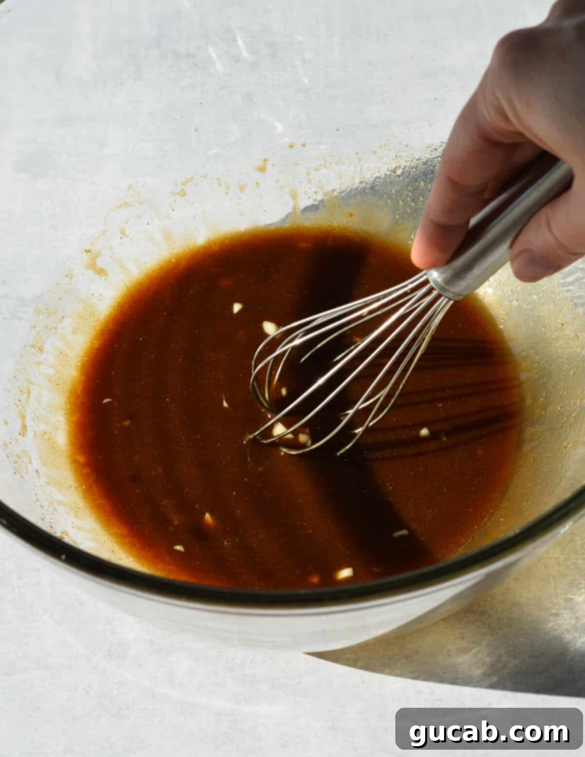A bowl of glossy balsamic marinade with a whisk in it, showing the perfectly emulsified mixture ready for chicken.