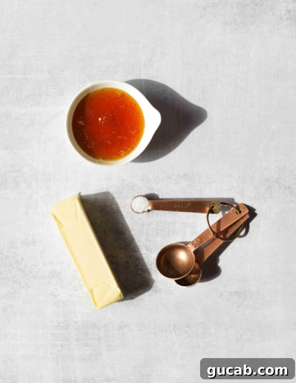A simple flat lay of the three key ingredients: a stick of unsalted butter, a jar of golden honey, and a small bowl of kosher salt.