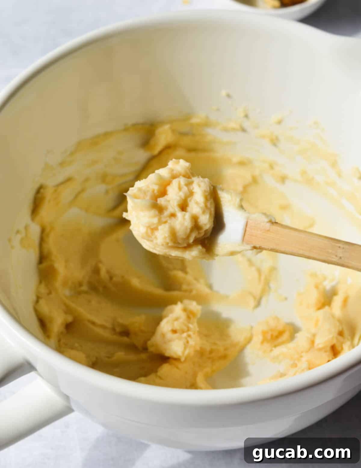 A small rubber spatula with a generous dollop of freshly made honey butter on its tip, showcasing its creamy texture.