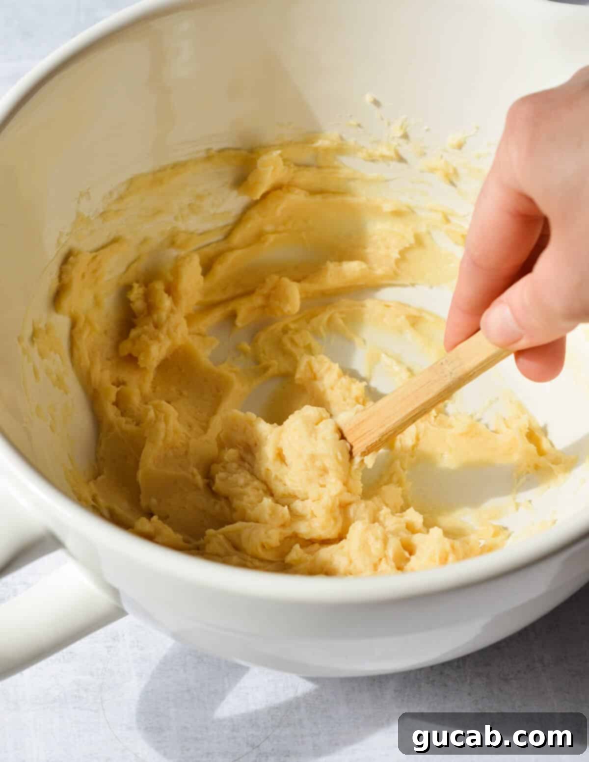 A hand stirring a bowl of smooth, creamy honey butter with a spatula, highlighting its perfect consistency.