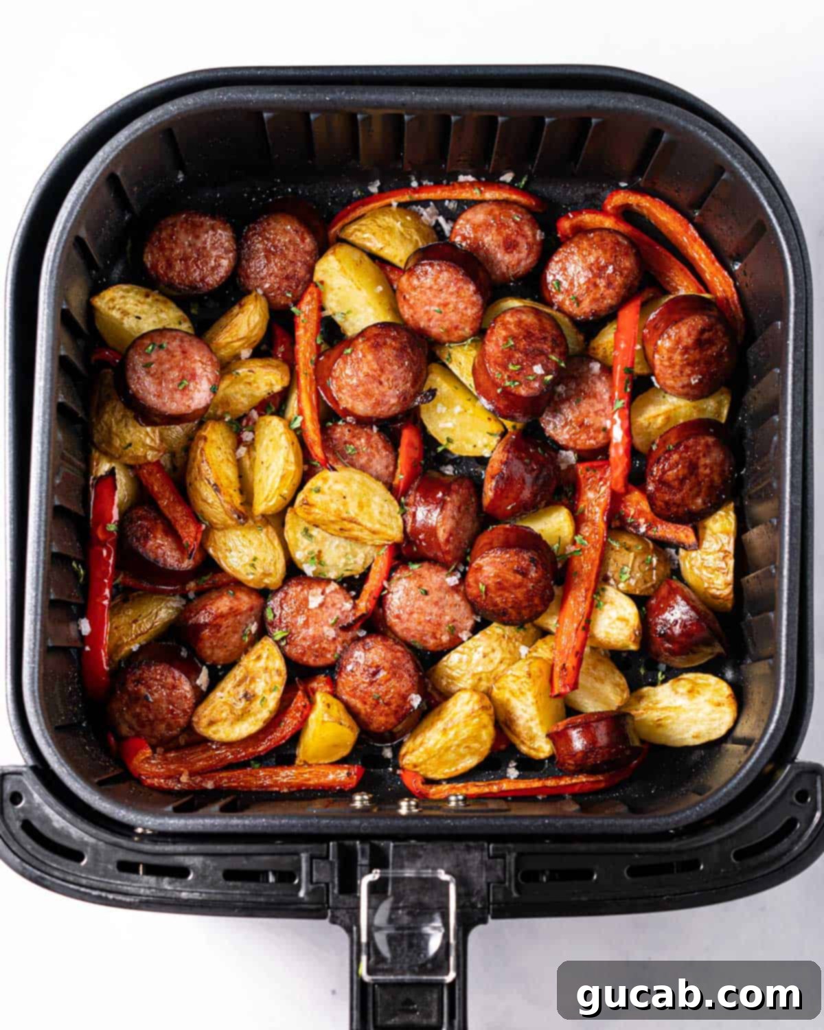 air fryer with kielbasa, potatoes, and red pepper in it. 