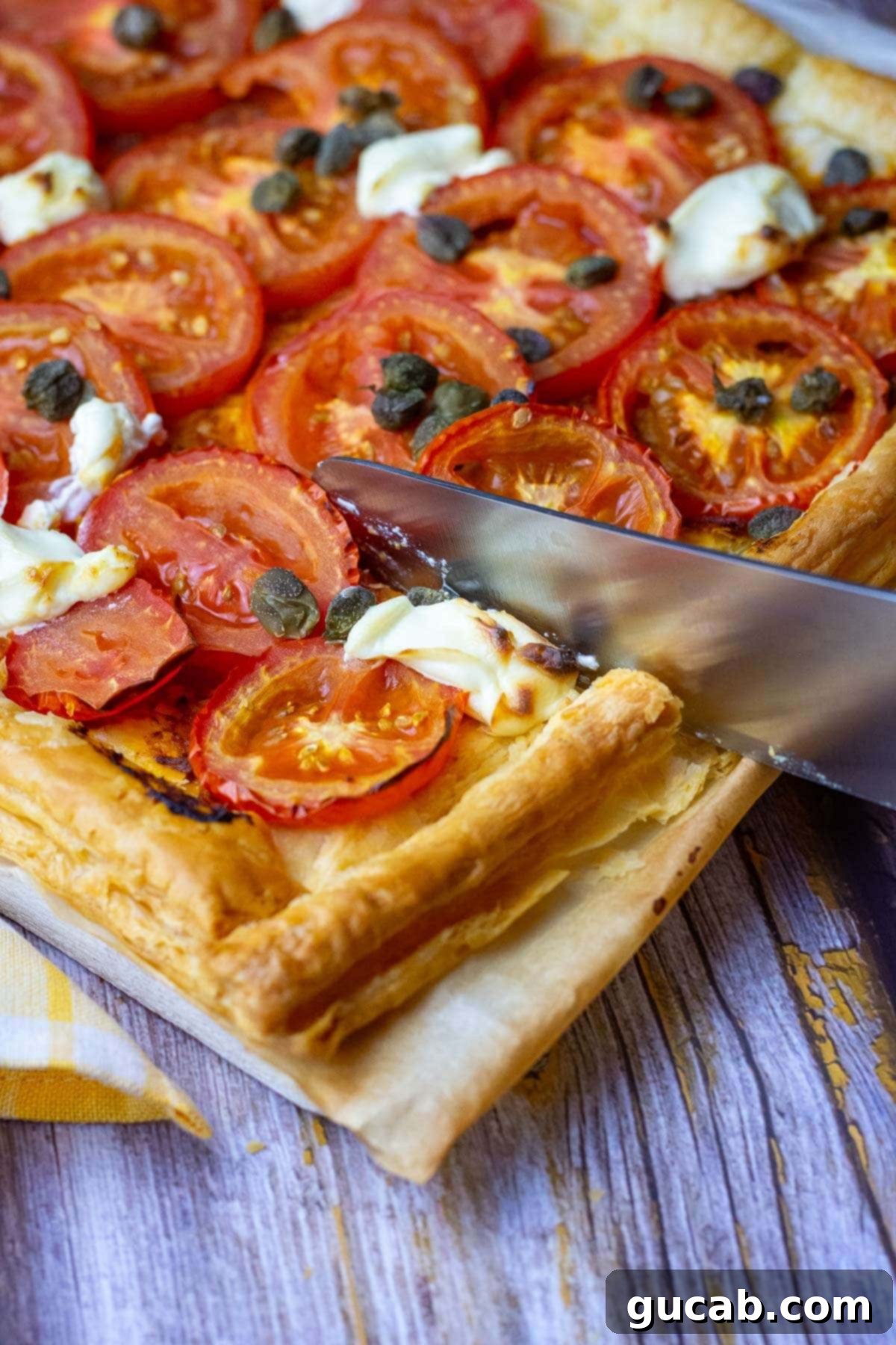 tomato puff pastry tart getting cut into a slice. 