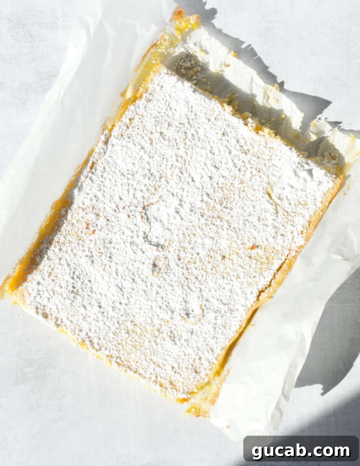 The uncut gluten-free key lime bar slab, lifted from the pan with parchment paper, ready for slicing.