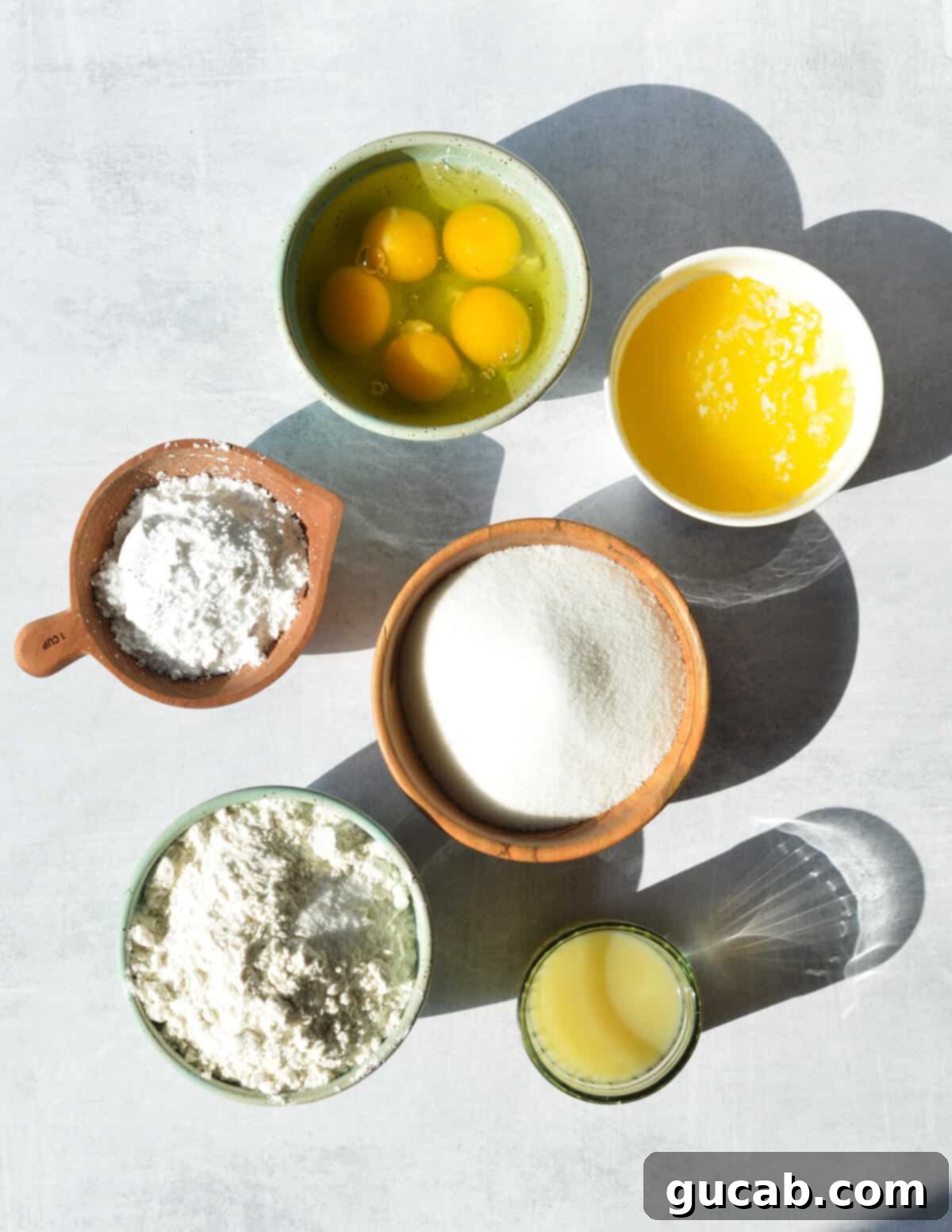 A collection of key ingredients for gluten-free key lime bars: eggs, gluten-free flour, key lime juice, granulated sugar, and powdered sugar, arranged for a clear visual guide.