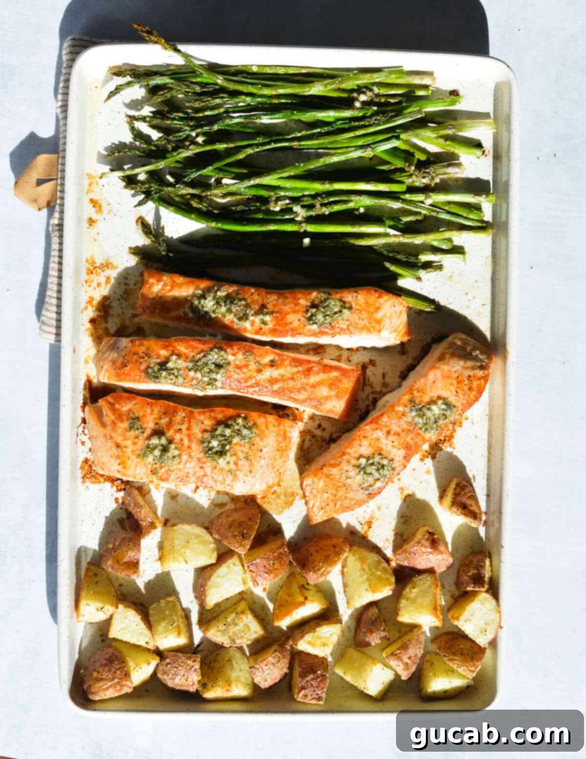 roasted asparagus, potatoes, and salmon on a sheet pan with lemon herb butter on top. 