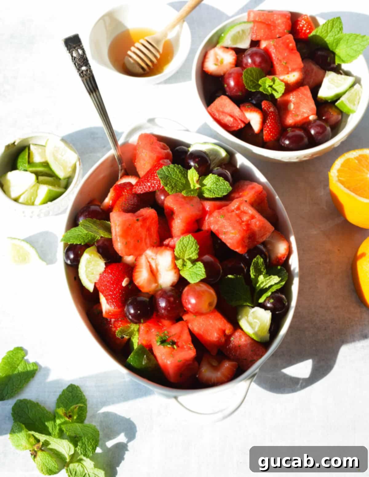 A vibrant bowl of watermelon, grapes, and strawberries, garnished with fresh mint and lime wedges, showcasing a refreshing summer fruit salad.
