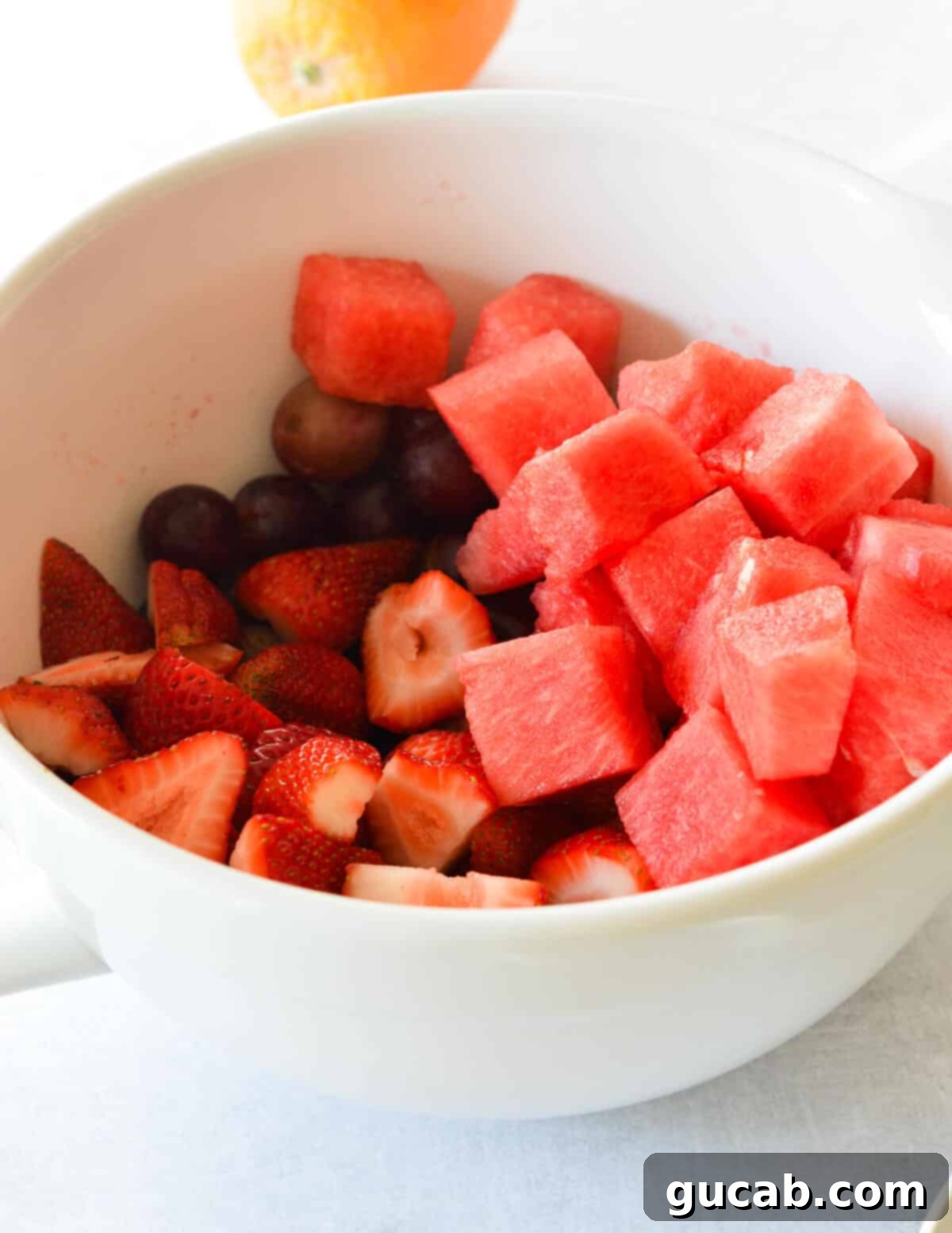 A large bowl filled with colorful chunks of watermelon, whole red grapes, and halved strawberries, perfectly prepped and ready for the dressing.