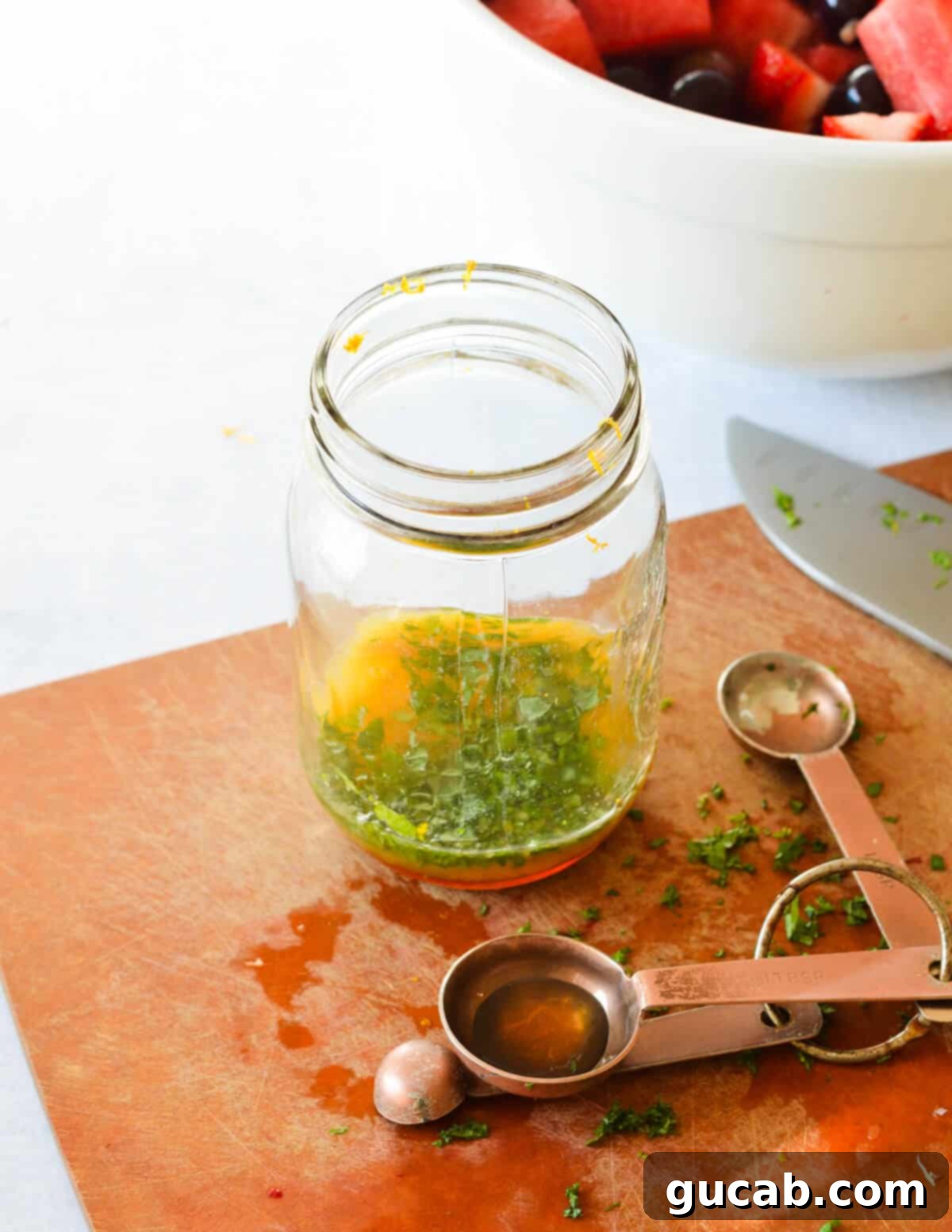 A mason jar filled with the liquid ingredients for the citrus mint dressing: orange juice, lime juice, honey, and fresh mint leaves, before shaking.