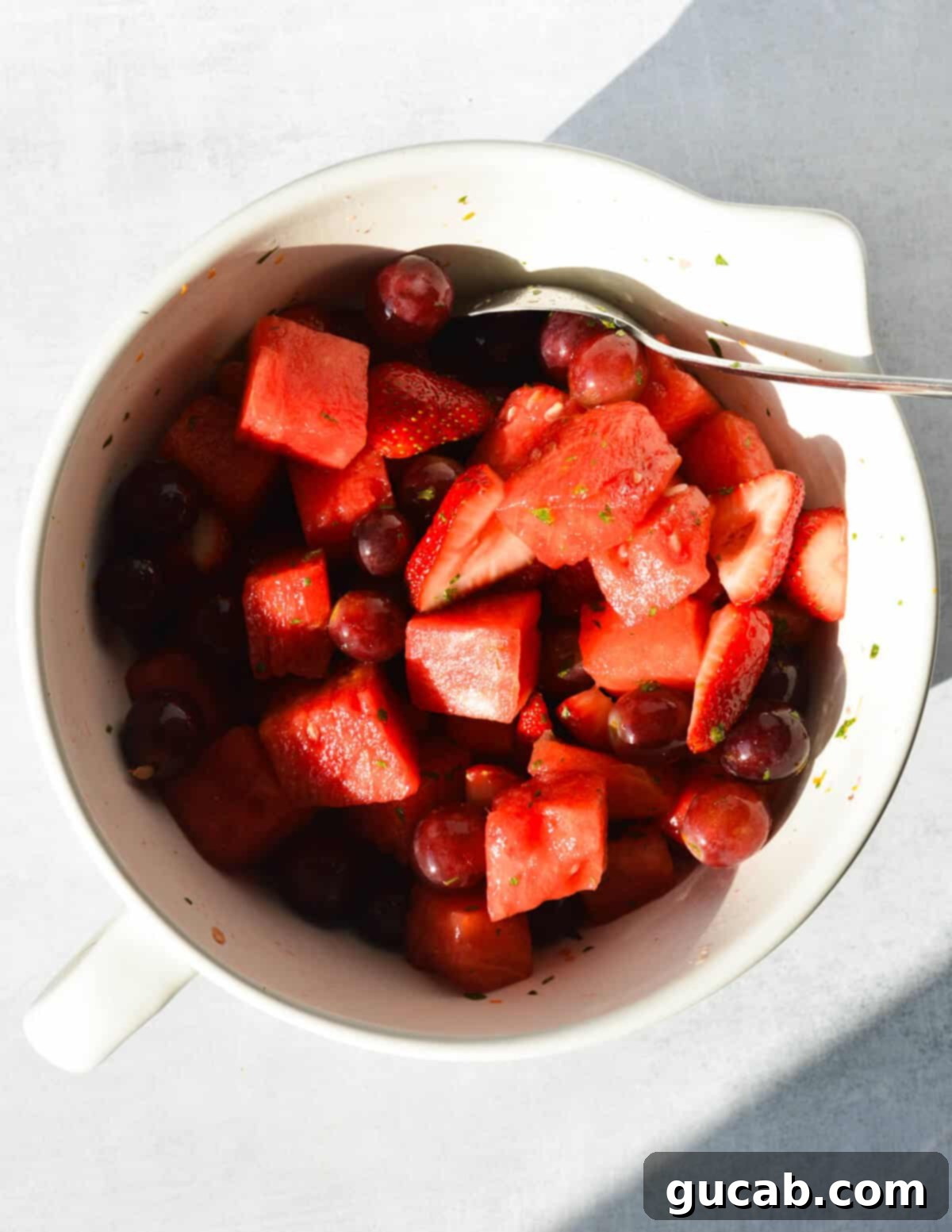 A large bowl of vibrant watermelon chunks, glistening red grapes, and halved strawberries, perfectly coated in a refreshing citrus mint dressing and garnished with fresh mint leaves.