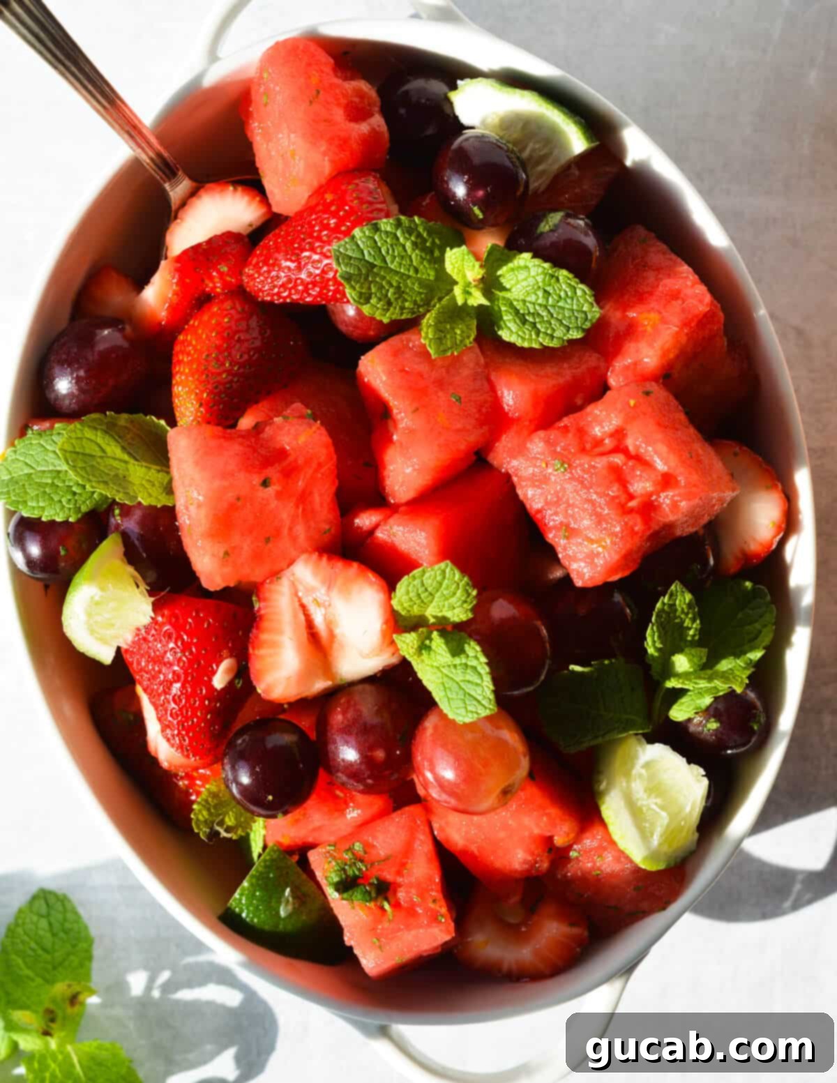 A large, overflowing bowl filled with colorful watermelon, red grapes, juicy strawberries, and garnished with fresh mint leaves, captured close-up and ready to be served as a delightful summer dish.