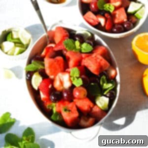 A beautifully presented bowl of watermelon fruit salad with grapes and strawberries, garnished with fresh mint leaves, ready to be served.