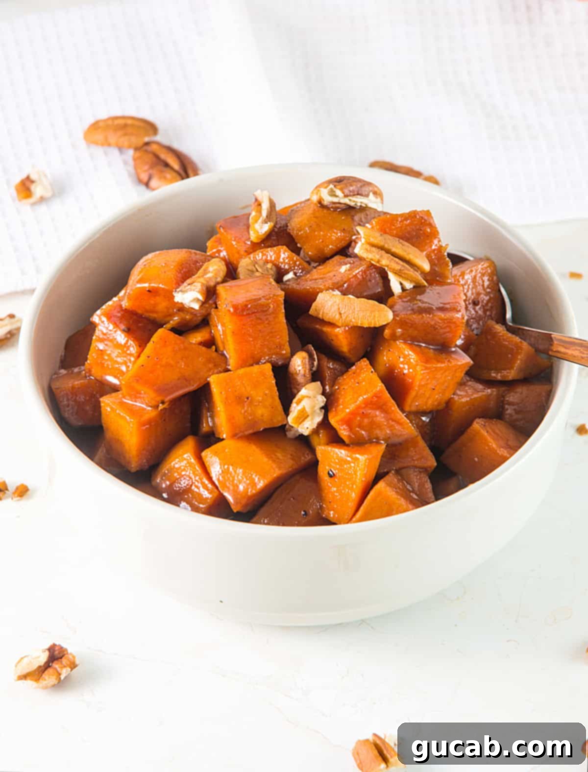 A beautiful bowl of candied sweet potatoes, shimmering with a buttery syrup and garnished with crunchy pecans, ready for a holiday feast.