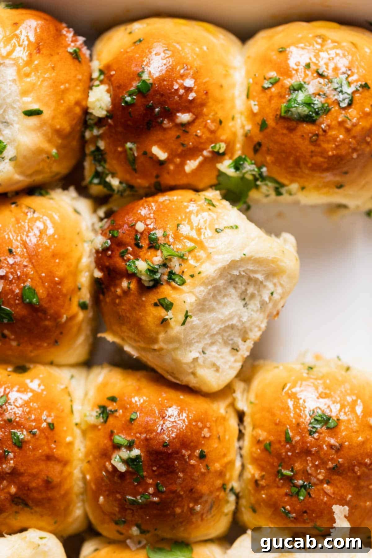 Warm, golden-brown garlic bread rolls, brushed with melted garlic butter and sprinkled with fresh parsley, ready to be pulled apart.