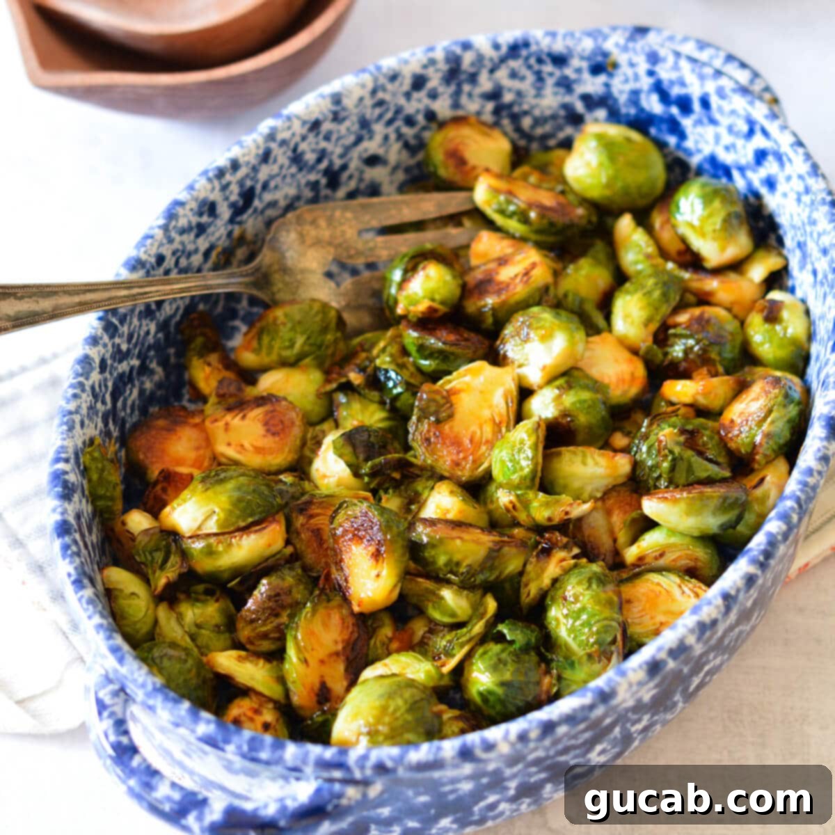 A serving dish brimming with perfectly pan-fried Brussels sprouts, coated in a glossy, sweet, and spicy sriracha honey sauce.