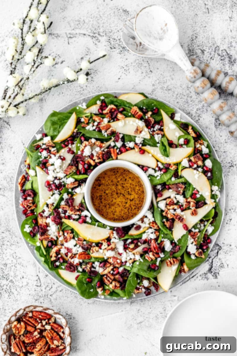 A festive spinach salad artfully arranged like a Christmas wreath, adorned with vibrant red pomegranate seeds, sliced green pears, and crumbled feta cheese.