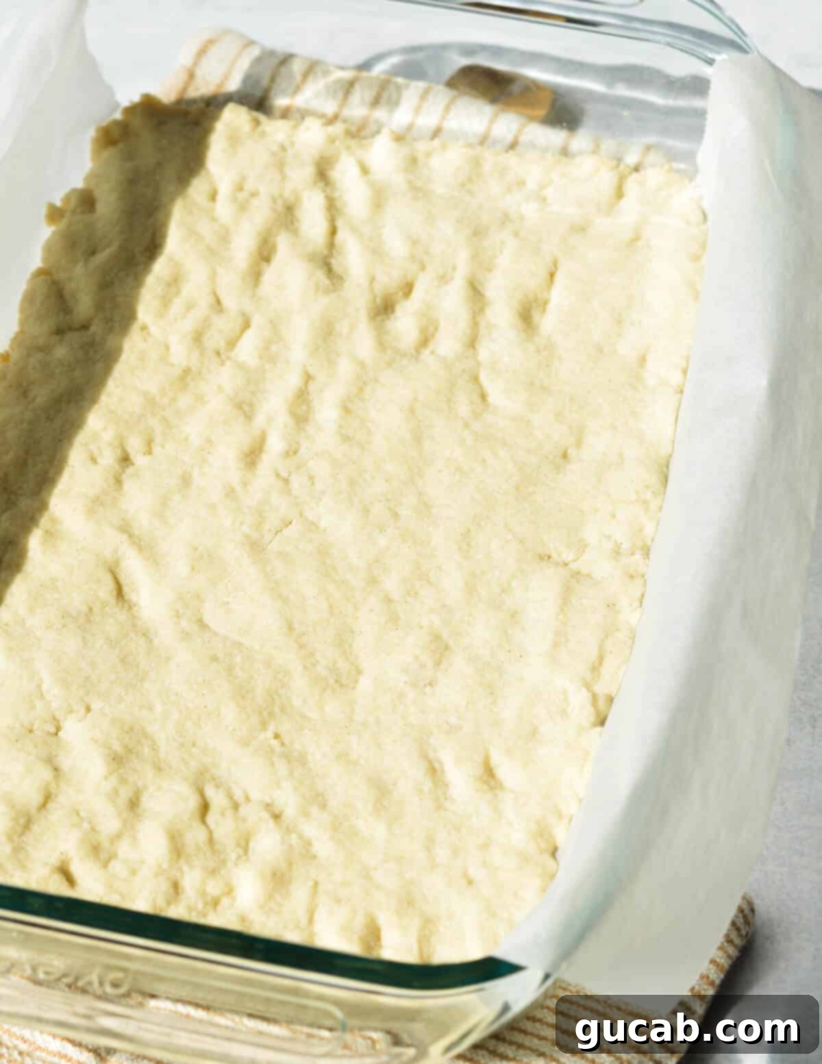 A golden-brown baked gluten-free shortbread crust in a parchment-lined baking dish, cooling.