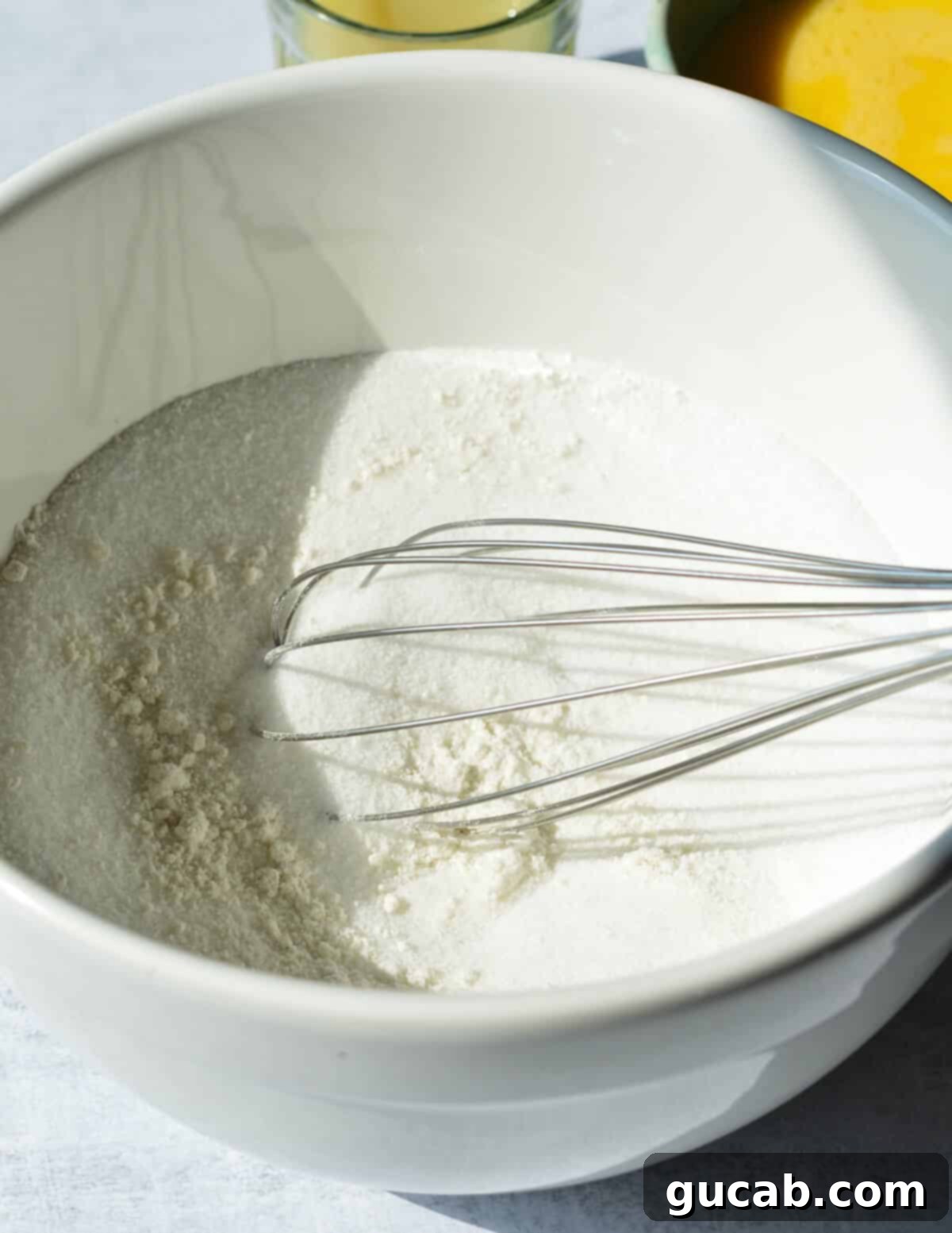 A bowl of granulated sugar and gluten-free flour with a whisk, ready to be combined for the lemon filling.