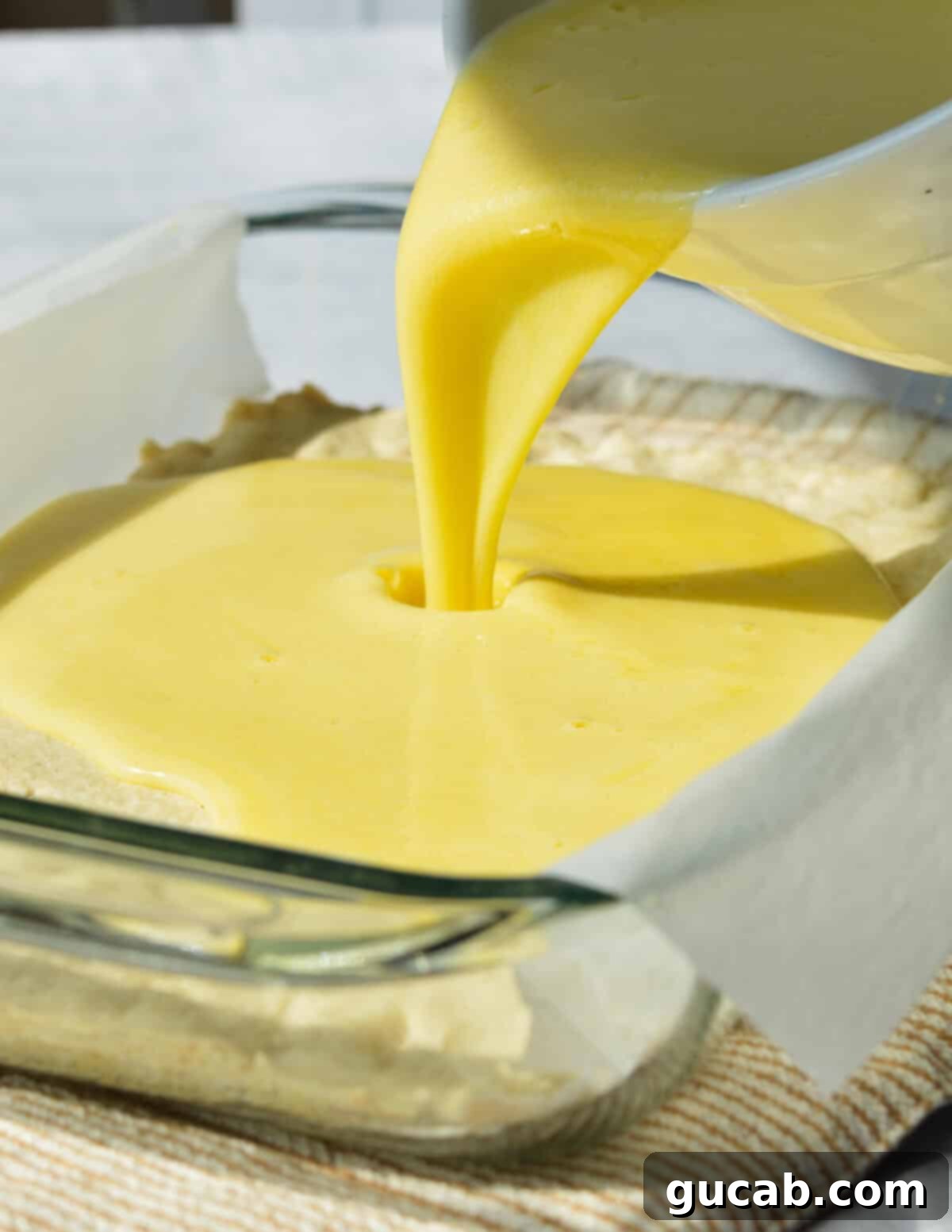 Pouring the smooth lemon filling into the pre-baked shortbread crust in a baking dish.