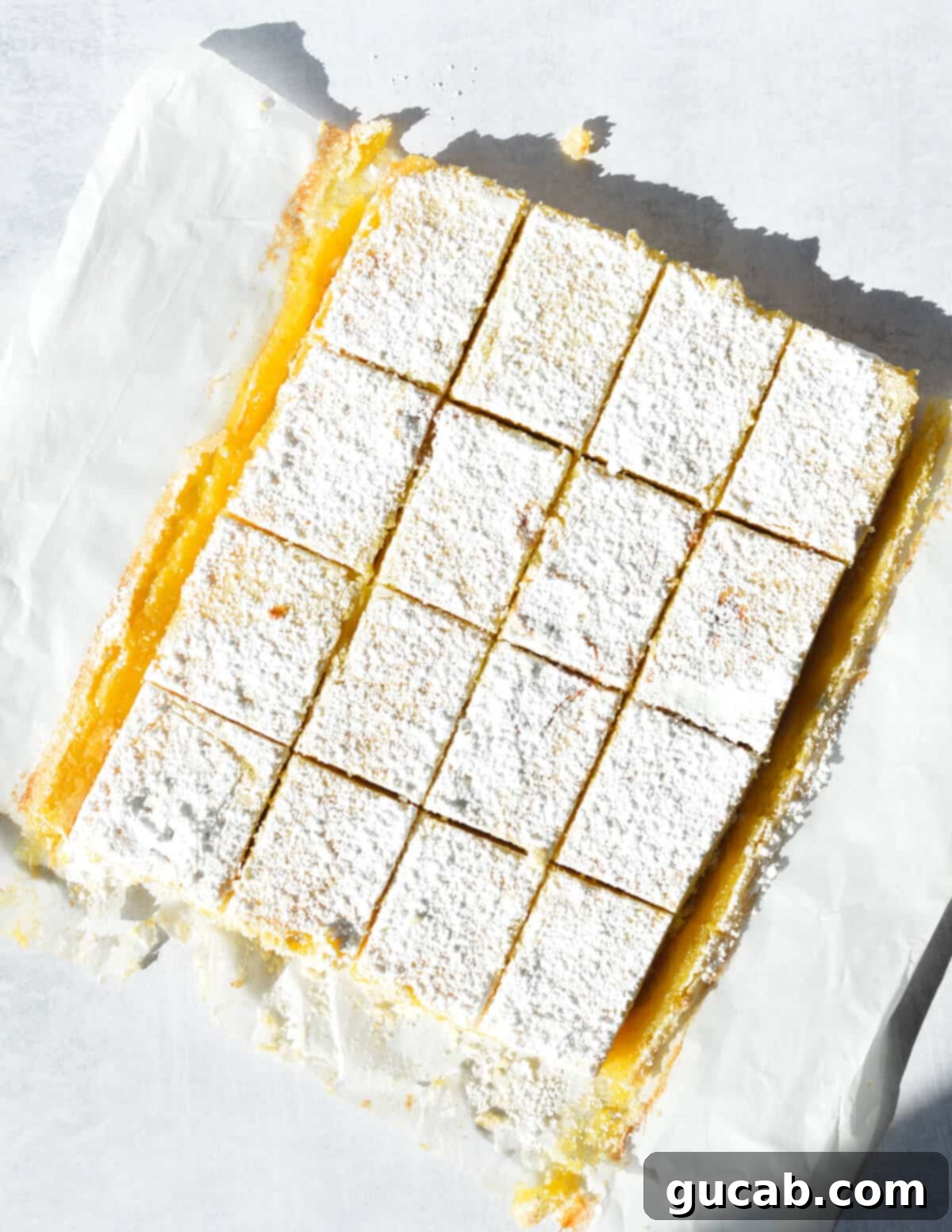 Neatly cut gluten-free lemon bars arranged on parchment paper, showcasing their perfect layers.