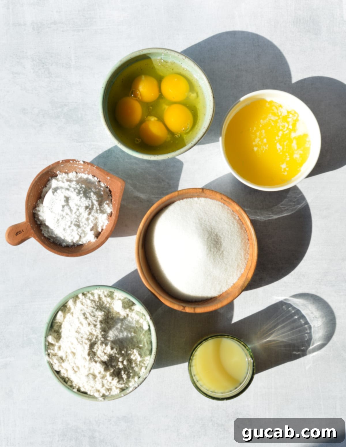 Close-up of key ingredients for gluten-free lemon bars: fresh eggs, unsalted butter, granulated sugar, powdered sugar, lemons, and a bag of gluten-free flour.