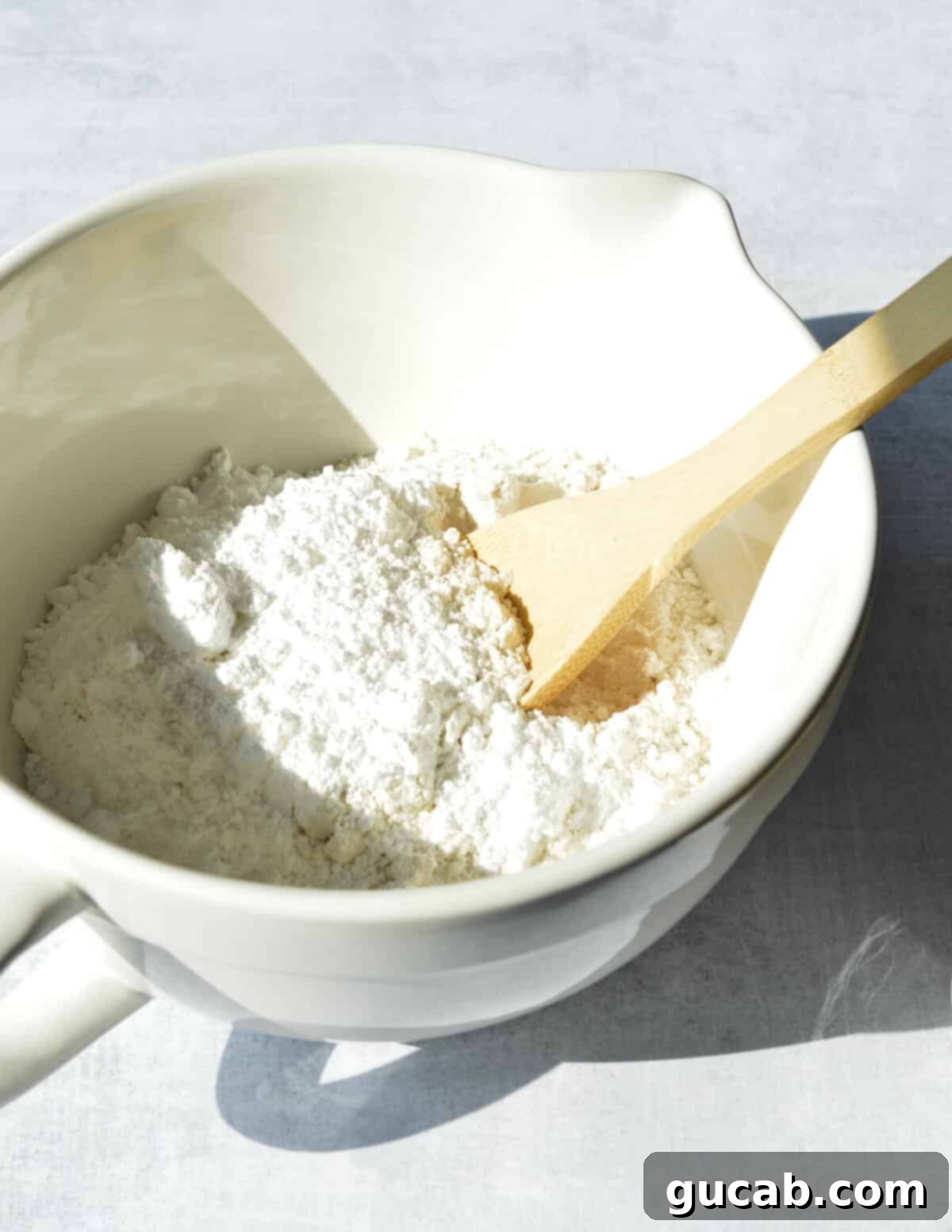 A close-up of gluten-free flour and powdered sugar being stirred together in a mixing bowl with a whisk.