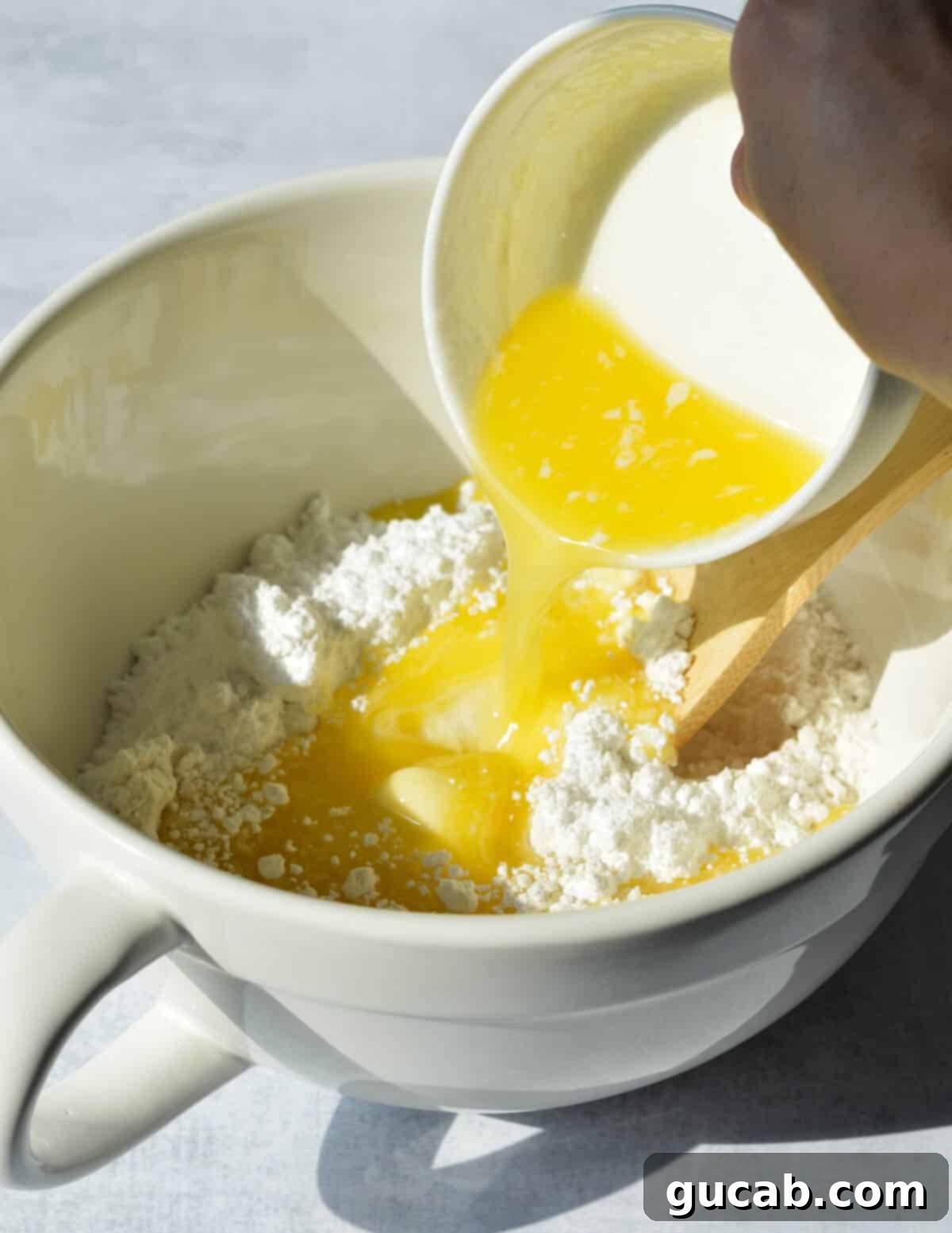 Melted unsalted butter being poured into a bowl containing gluten-free flour and sugar.
