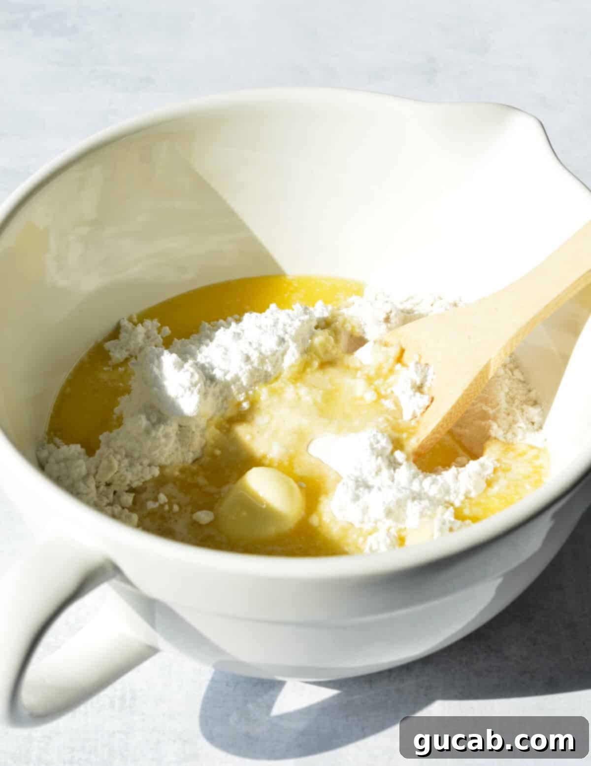 Mixing gluten-free flour, powdered sugar, and melted butter with a spoon to form a shortbread dough.