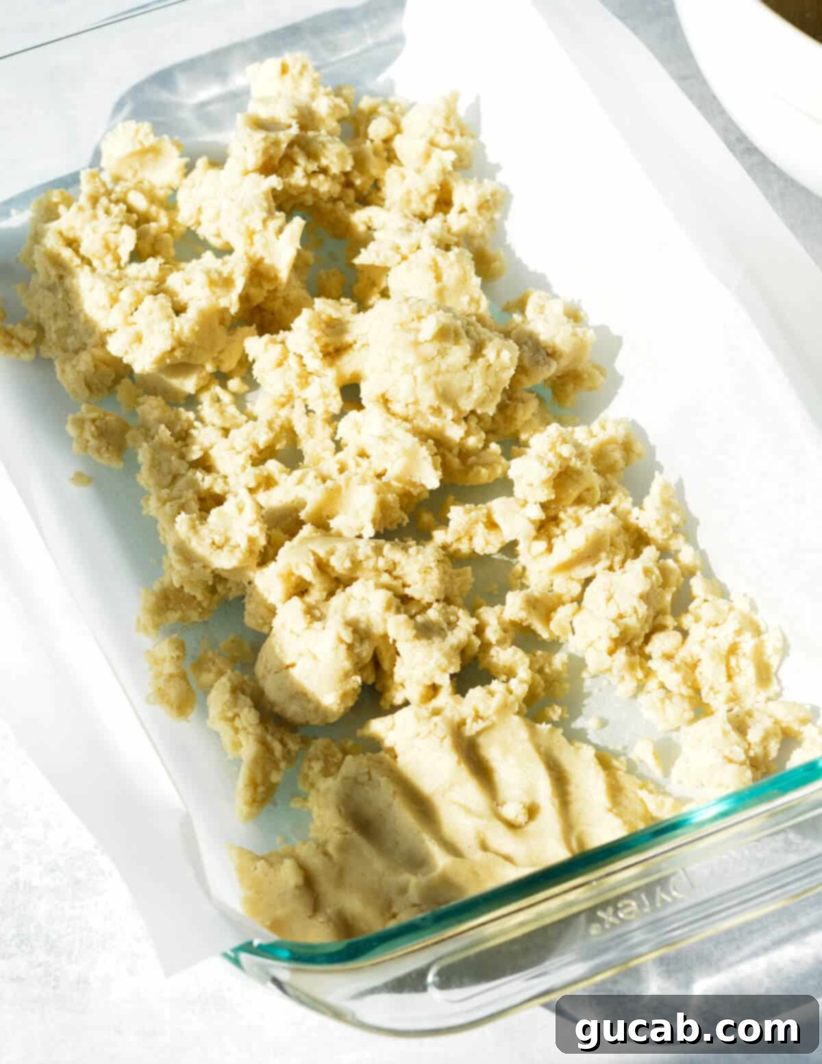 Gluten-free shortbread dough pressed into a baking dish lined with parchment paper.