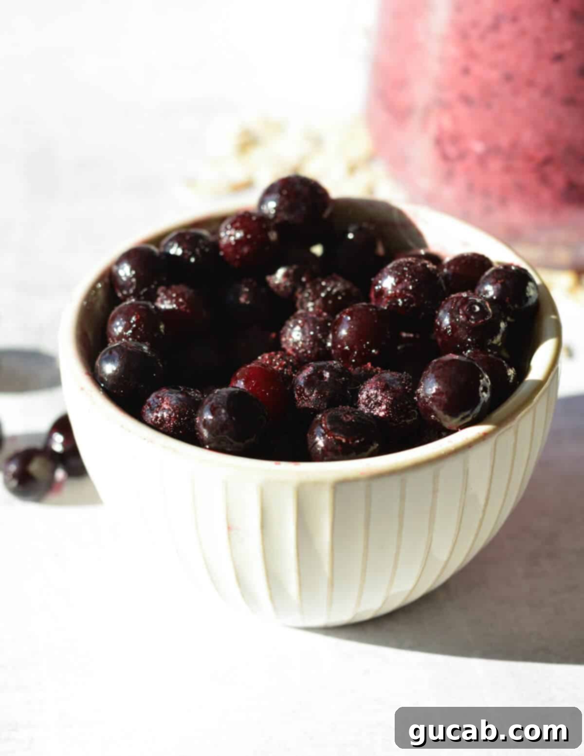 A clear glass bowl filled to the brim with perfectly frozen blueberries, their frosty coating glistening.