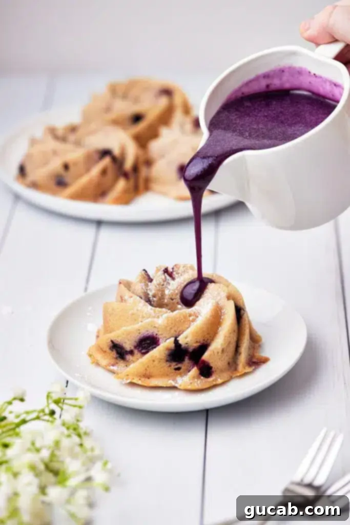 A close-up shot of a hand drizzling a luscious blueberry glaze over a mini blueberry bundt cake.