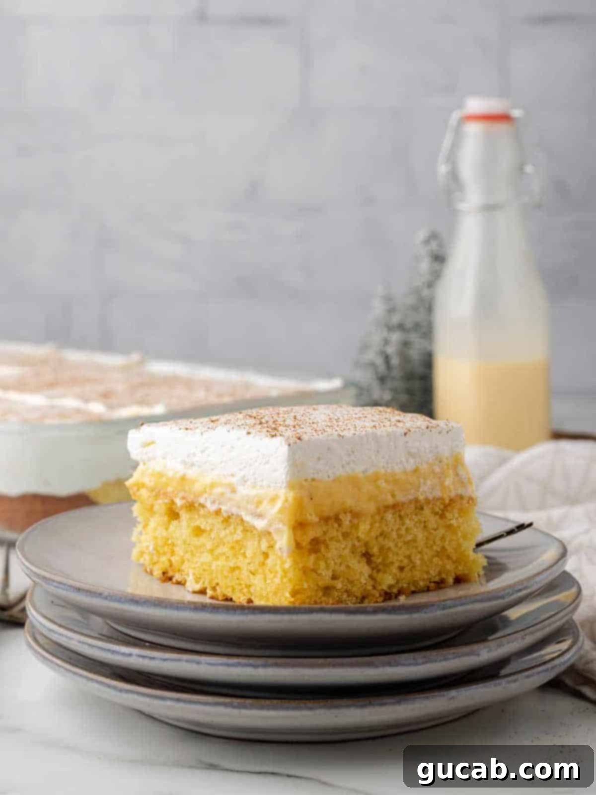 A slice of moist eggnog poke cake on a white plate, topped with whipped cream and a sprinkle of nutmeg, ready to be enjoyed.