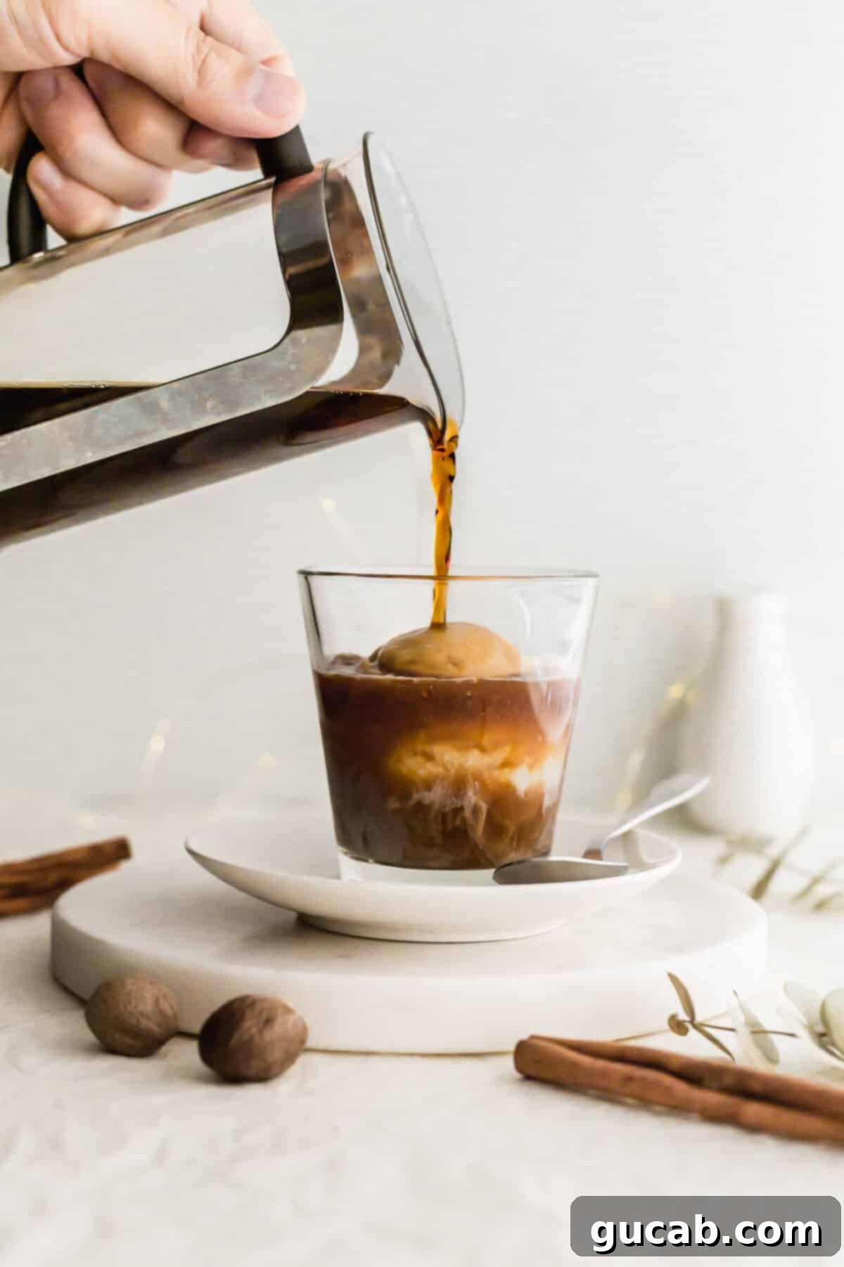 Hot coffee being poured over a scoop of creamy eggnog ice cream in a clear glass, creating a beautiful eggnog affogato.