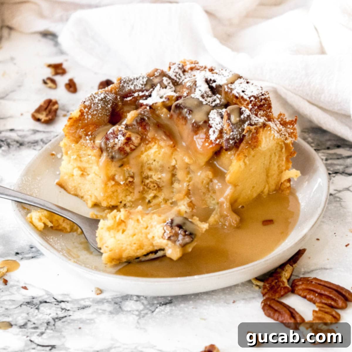 A warm slice of eggnog bread pudding, glistening with a generous drizzle of rich brown butter rum sauce, served on a plate.