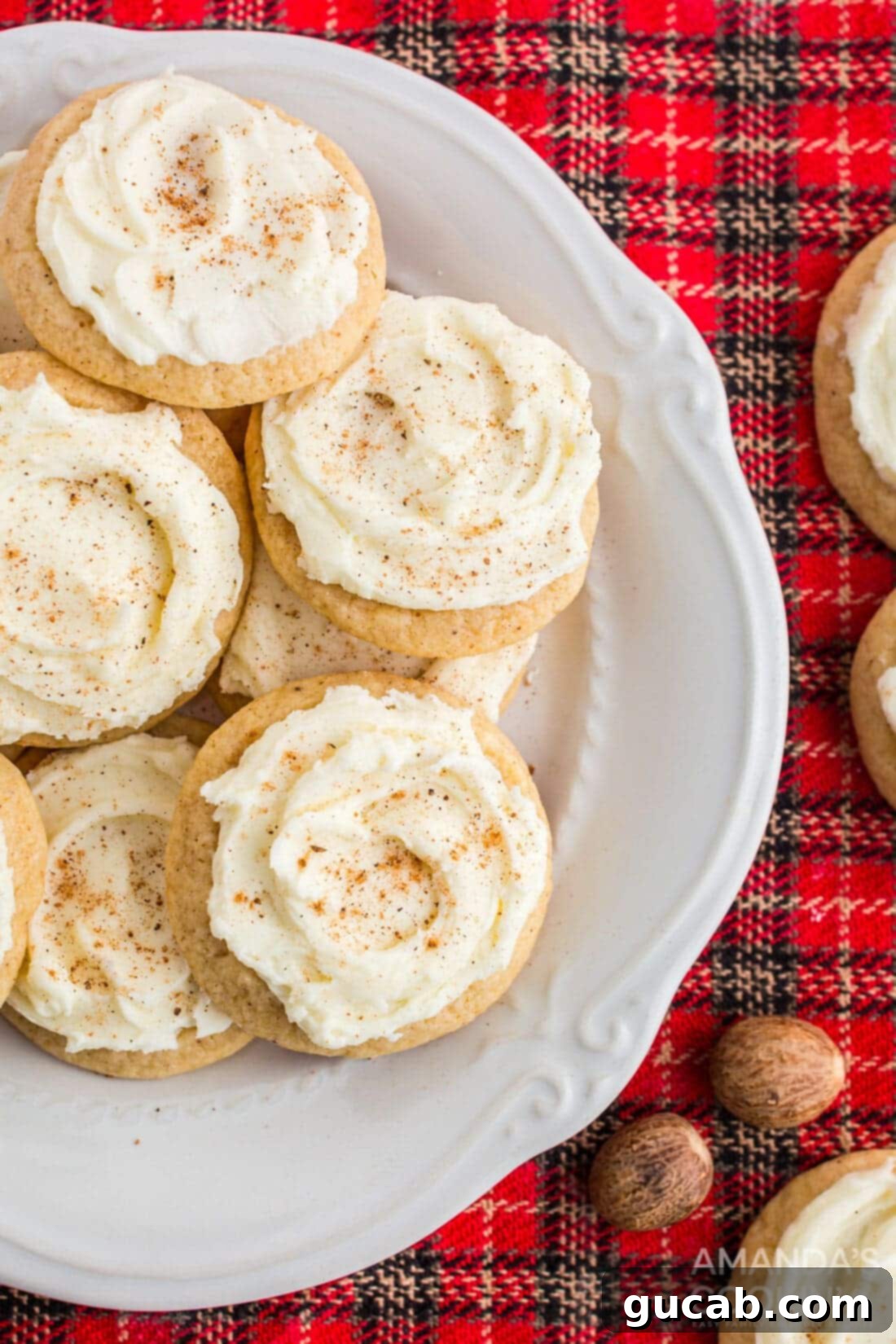 A plate piled high with soft, frosted eggnog cookies, each topped with a sprinkle of nutmeg, inviting a bite.