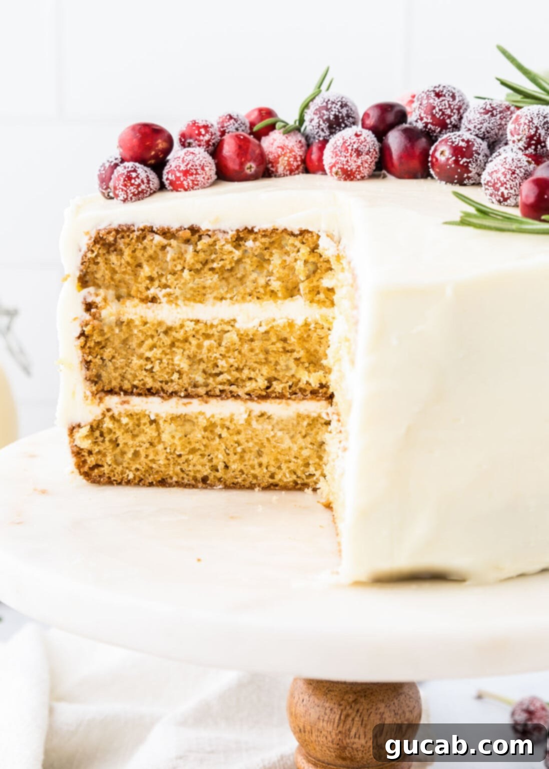 A magnificent eggnog layer cake with a slice removed, revealing its moist layers and creamy frosting, adorned with sugared cranberries.