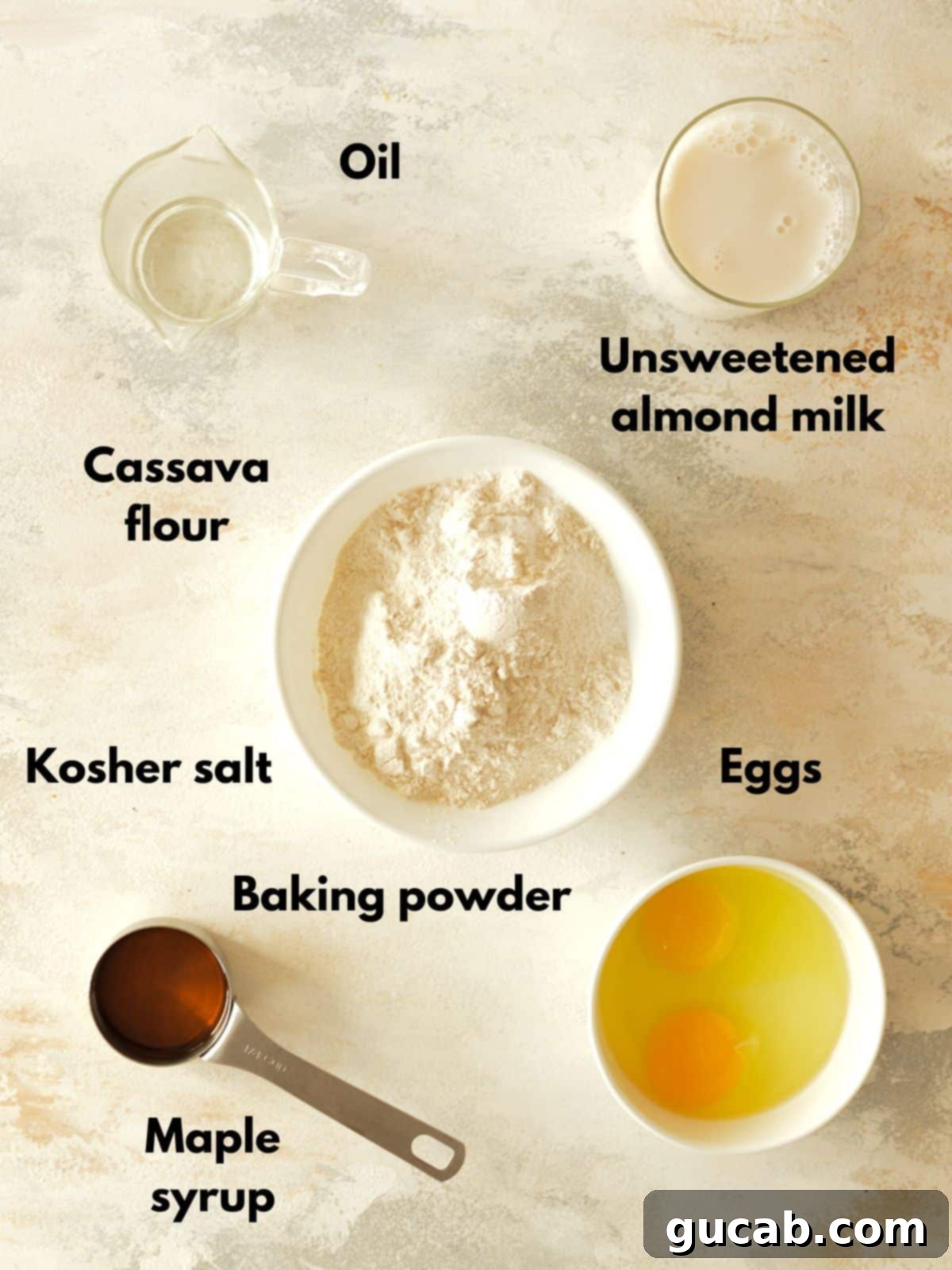 A selection of ingredients laid out, including cassava flour, almond milk, eggs, and maple syrup, ready for making pancakes.