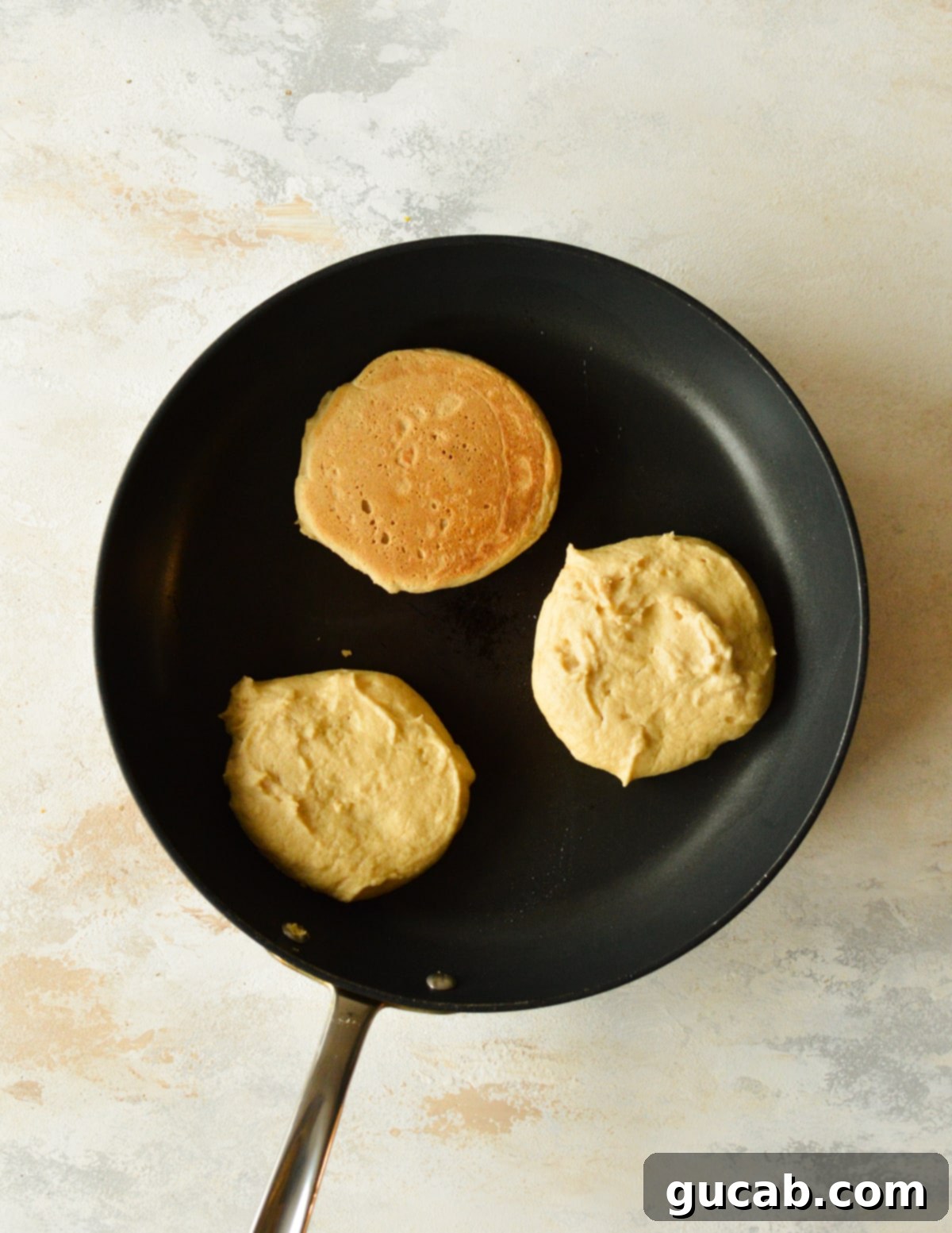Three cassava flour pancakes cooking in a nonstick skillet.