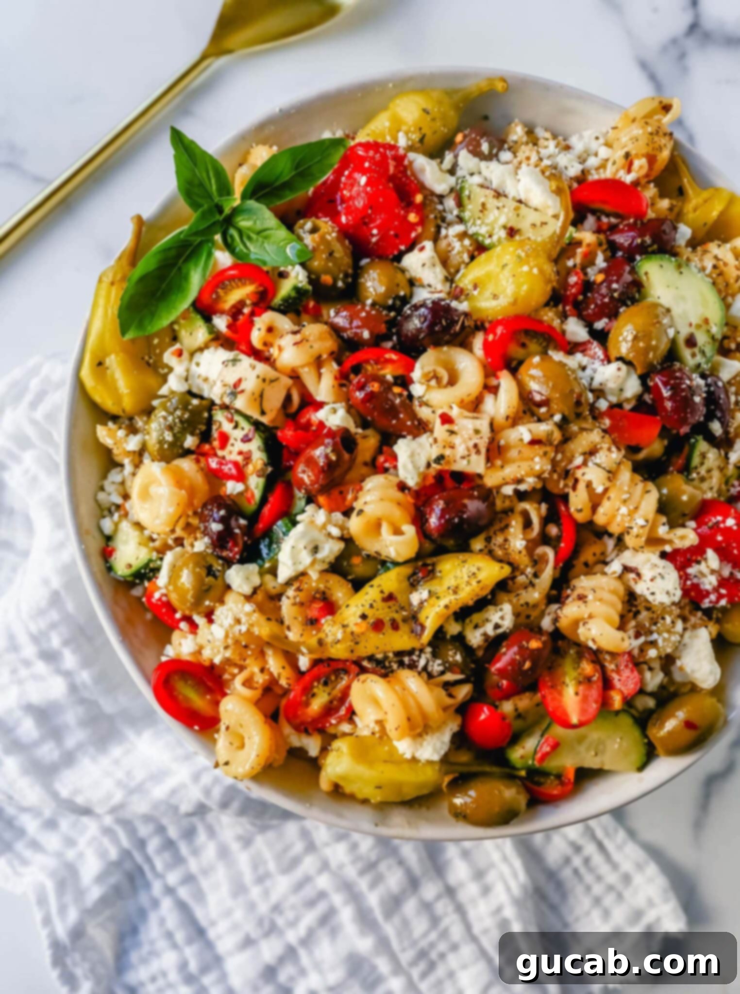 A large, enticing bowl of Greek pasta salad, richly garnished with black olives, crumbled feta cheese, and fresh vegetables.